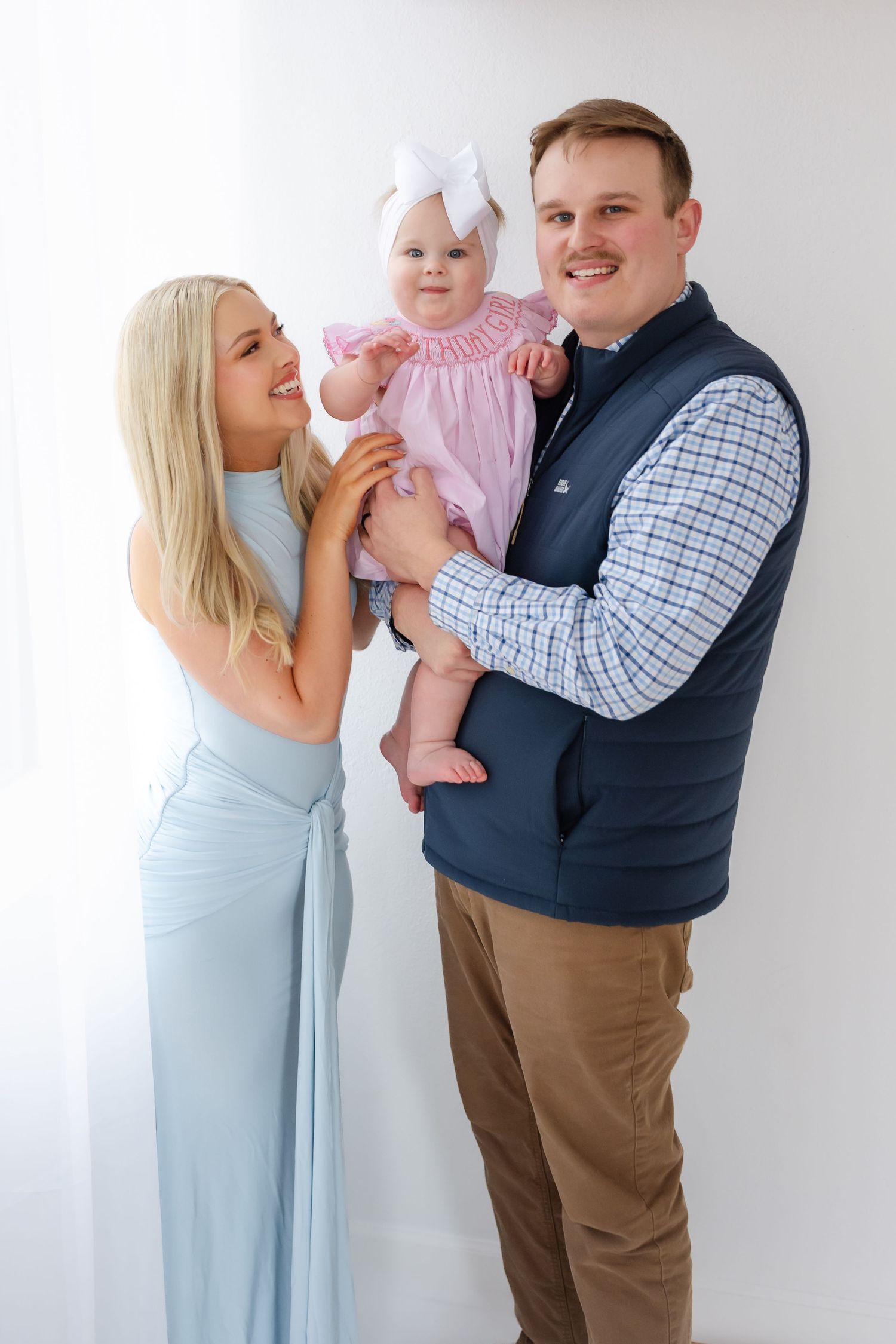 A family in coordinated blue and pink outfits poses together against a white wall in a series of candid moments.