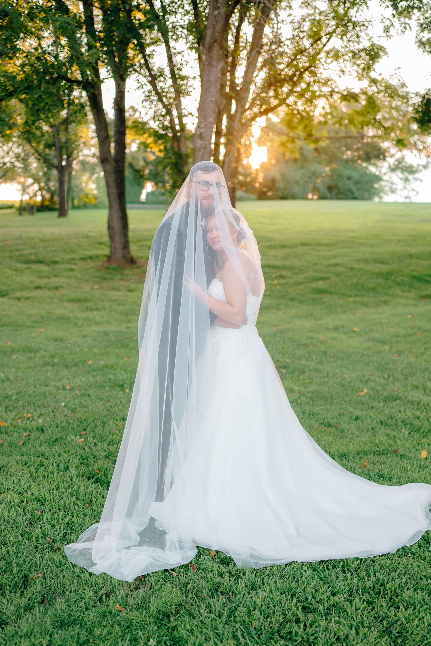 Ethereal wedding dress and veil photos in a sunlit grassy field.