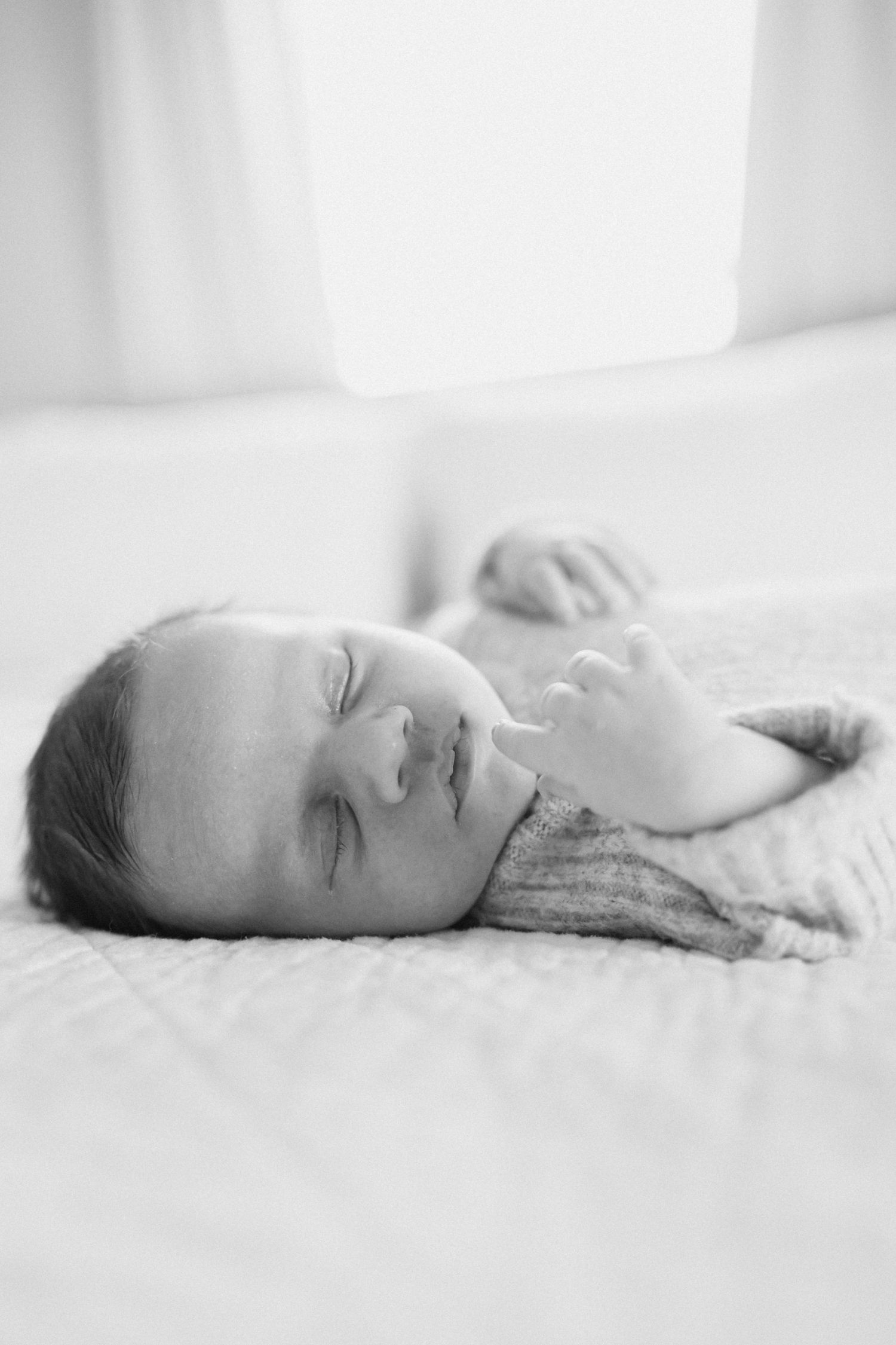 Peaceful newborn sleeping on white textured bedding in black and white photography.