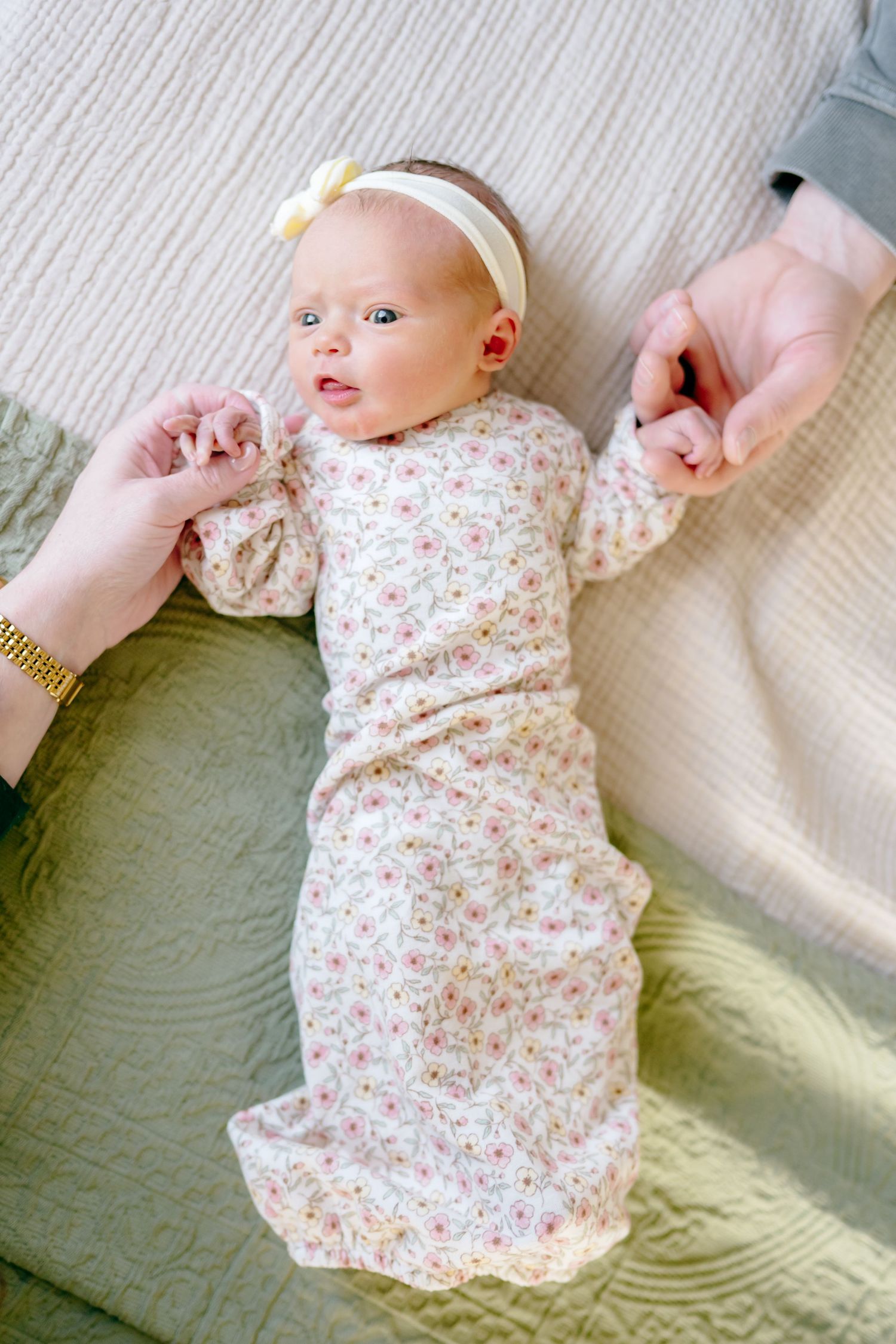Baby in floral dress lies on textured cream blanket during lifestyle photoshoot.
