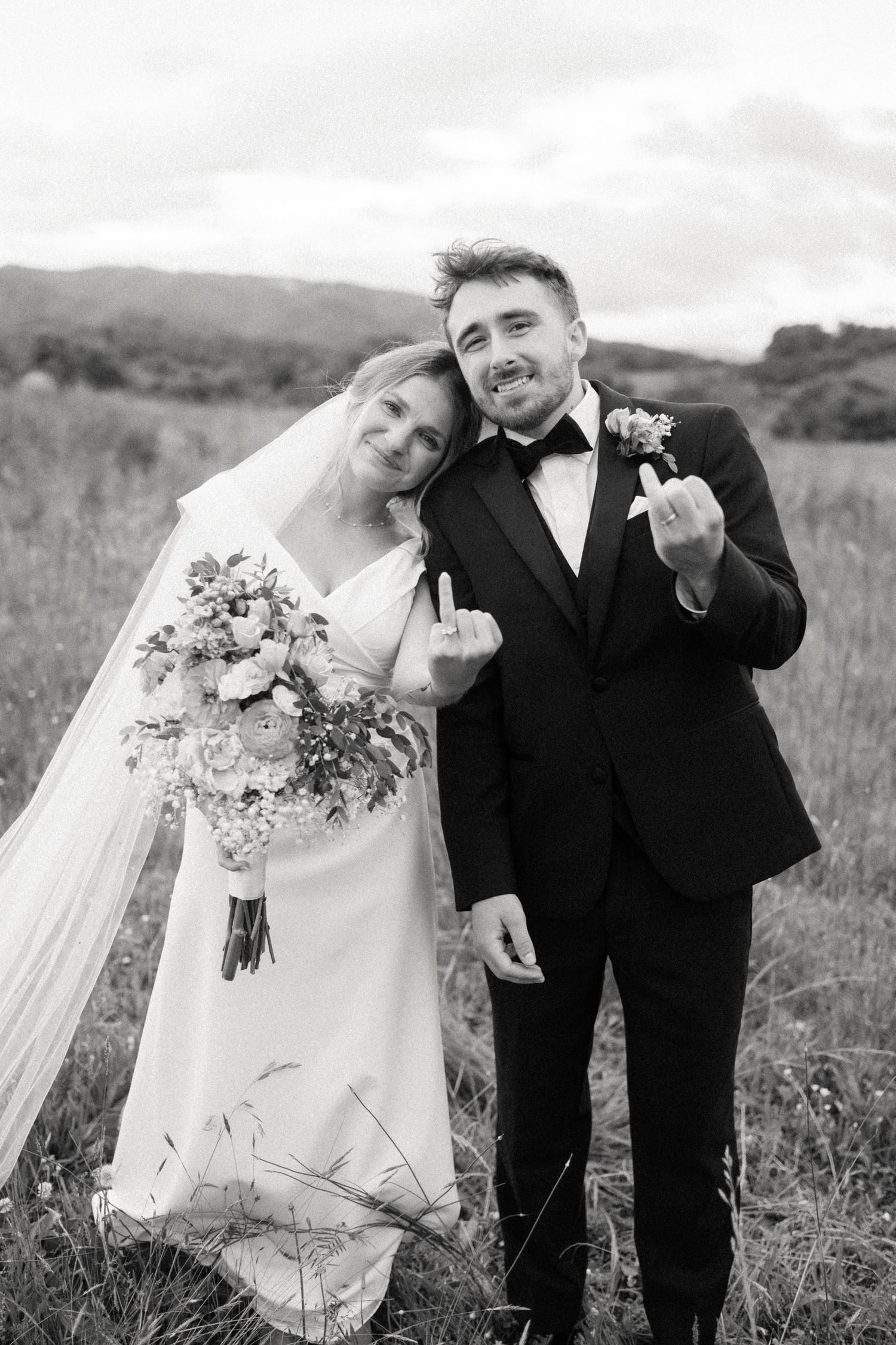Candid black and white portrait of newlyweds dancing in field.
