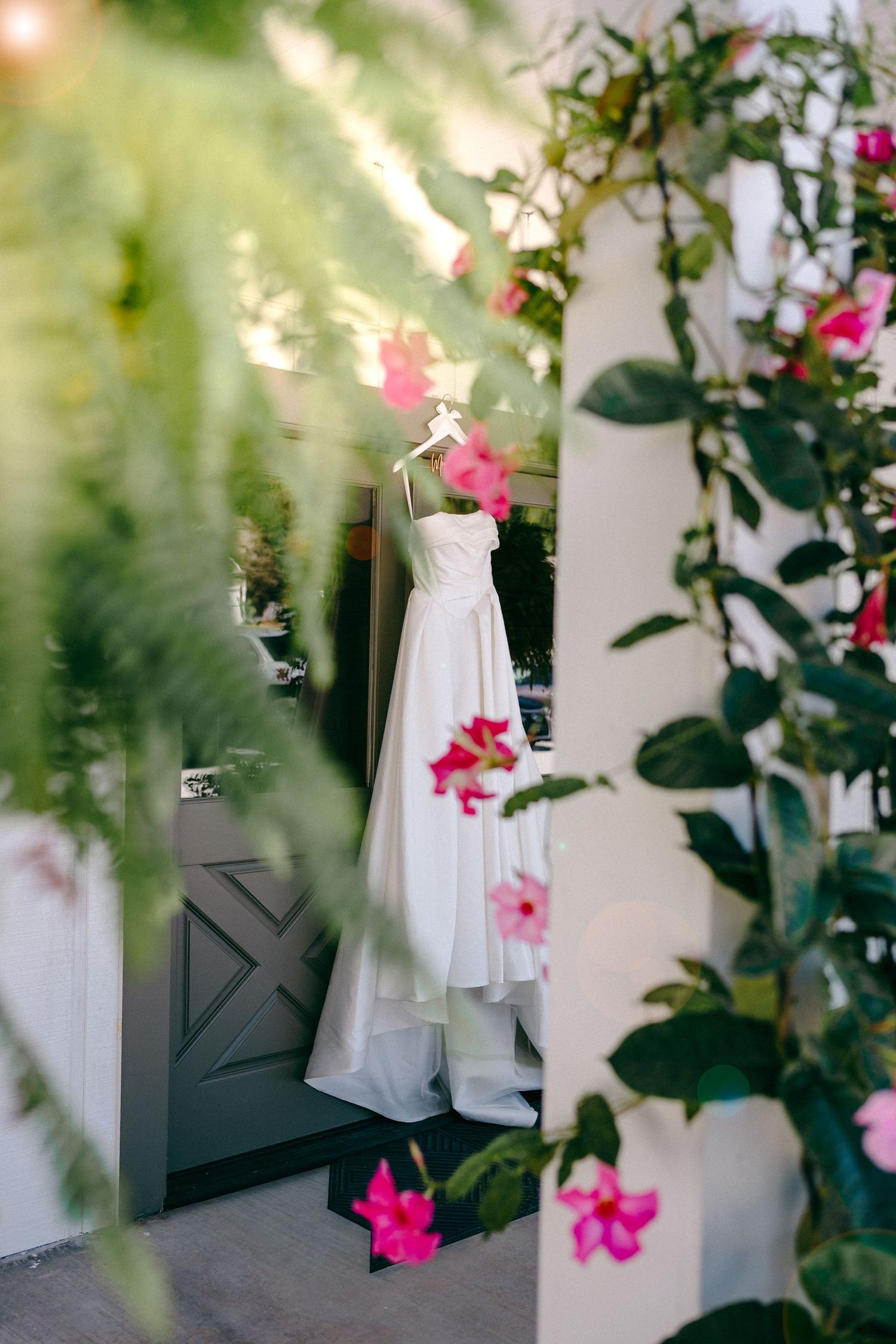 White wedding dress hanging among pink bougainvillea flowers and greenery.