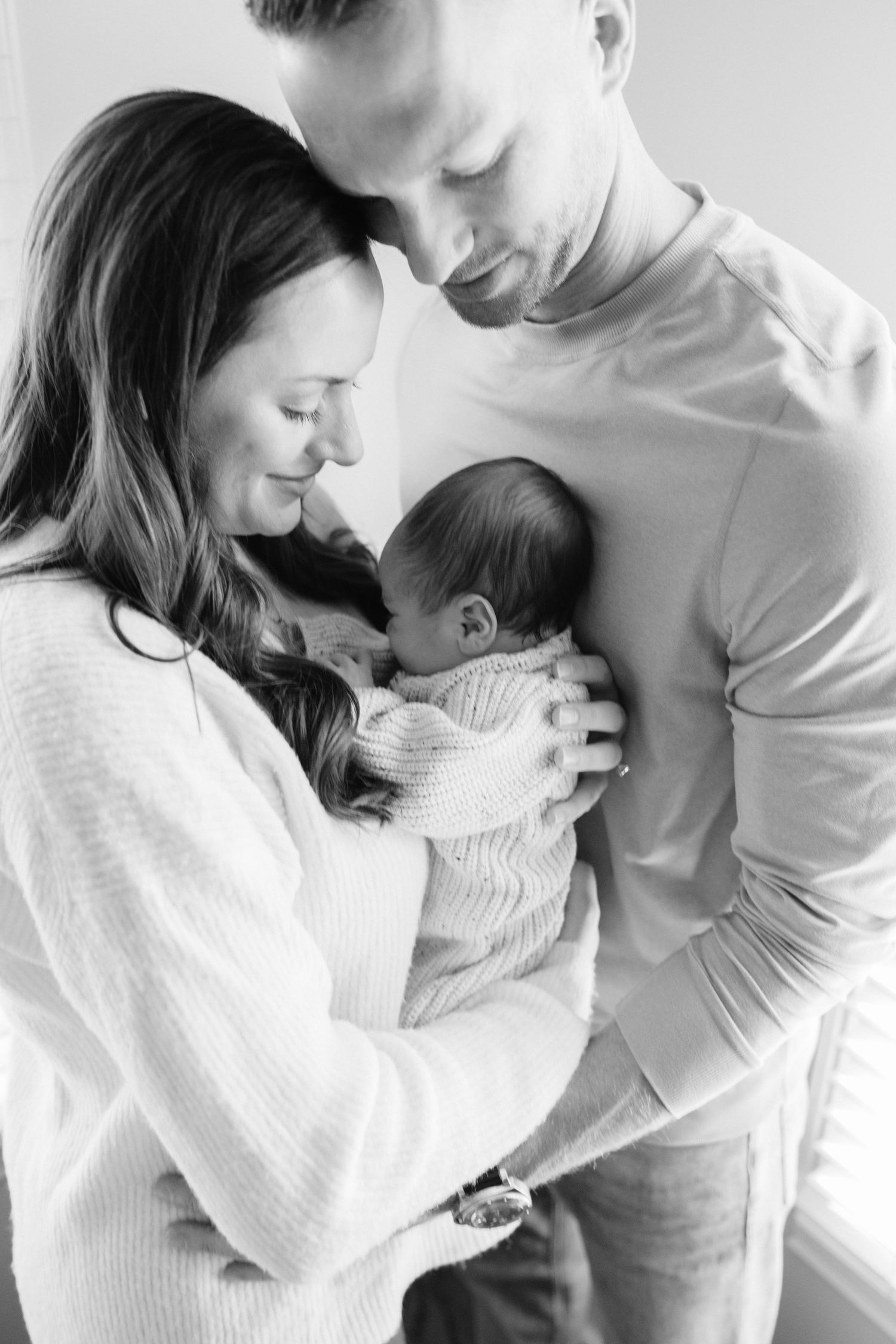Family shares intimate moment with newborn baby in white room.