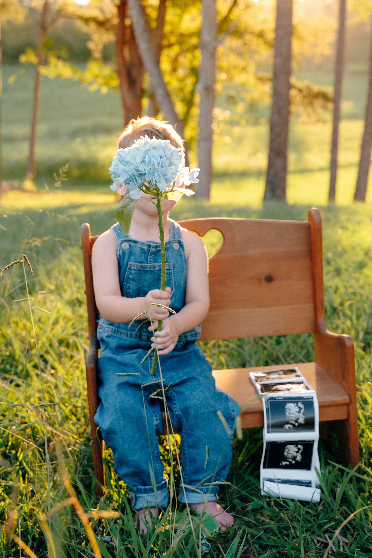 Child in overalls sits on wooden bench outdoors with ultrasound photos.
