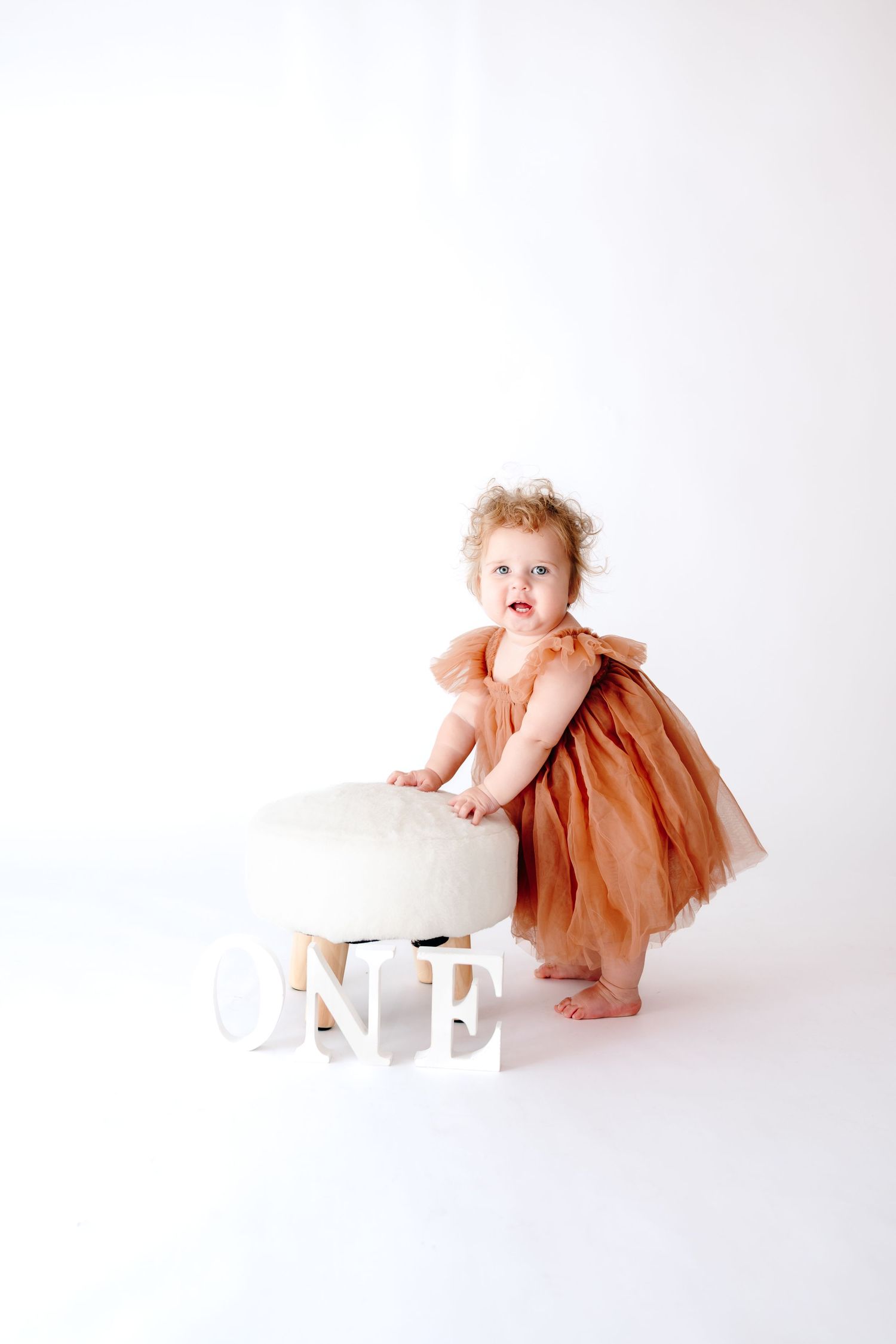 Baby in peach tulle dress explores white block letters on white background.