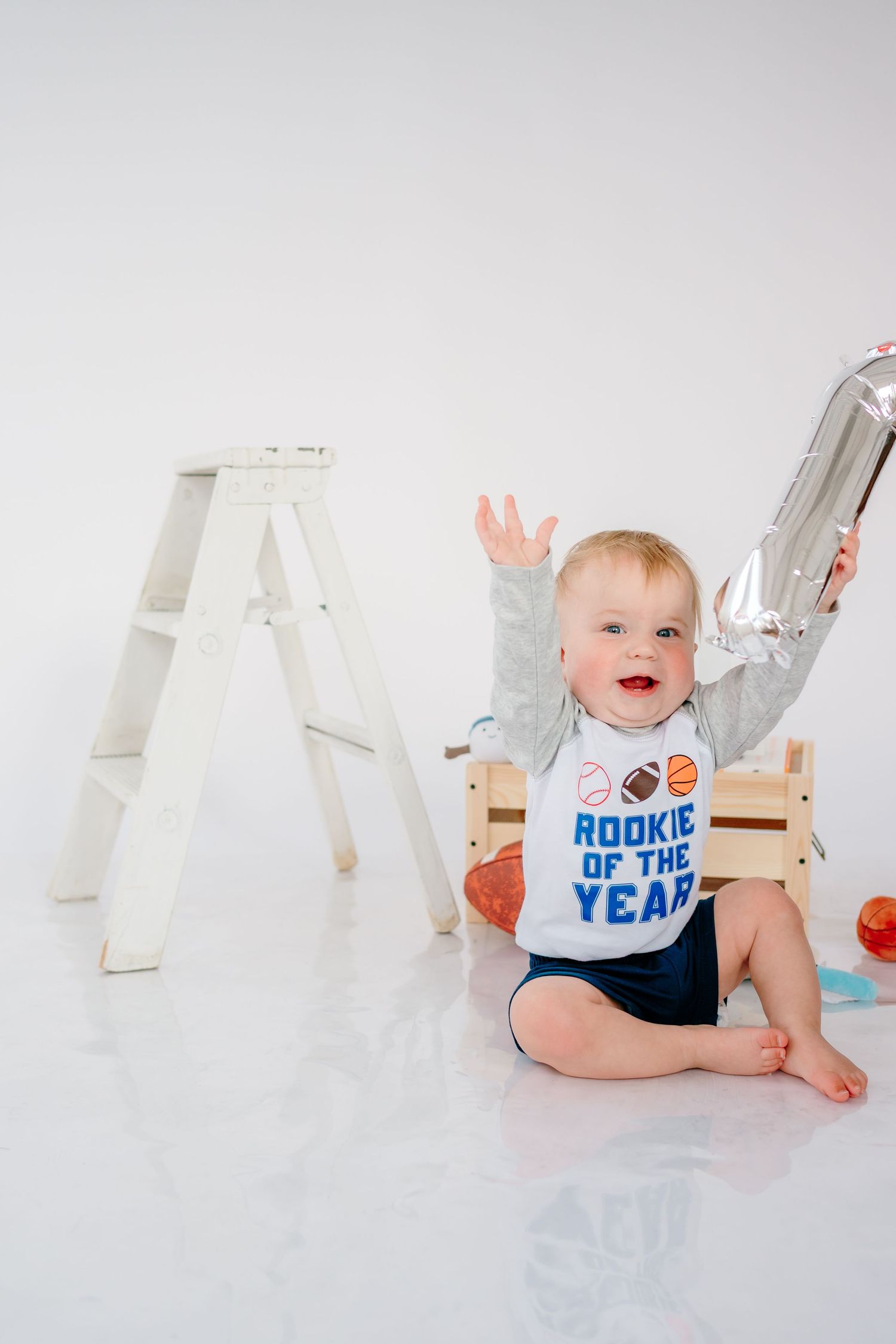 Baby wearing sports-themed onesie crawling near white letters against white background.