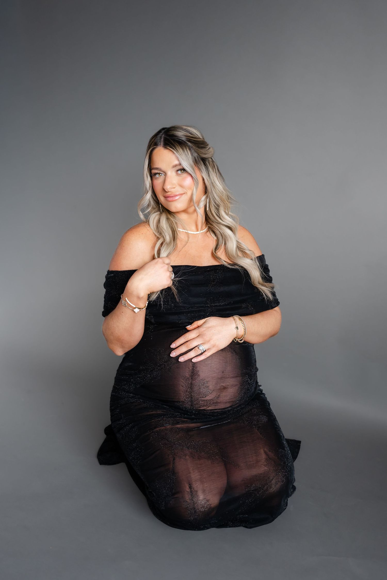 Studio maternity portrait with woman in black off-shoulder dress.