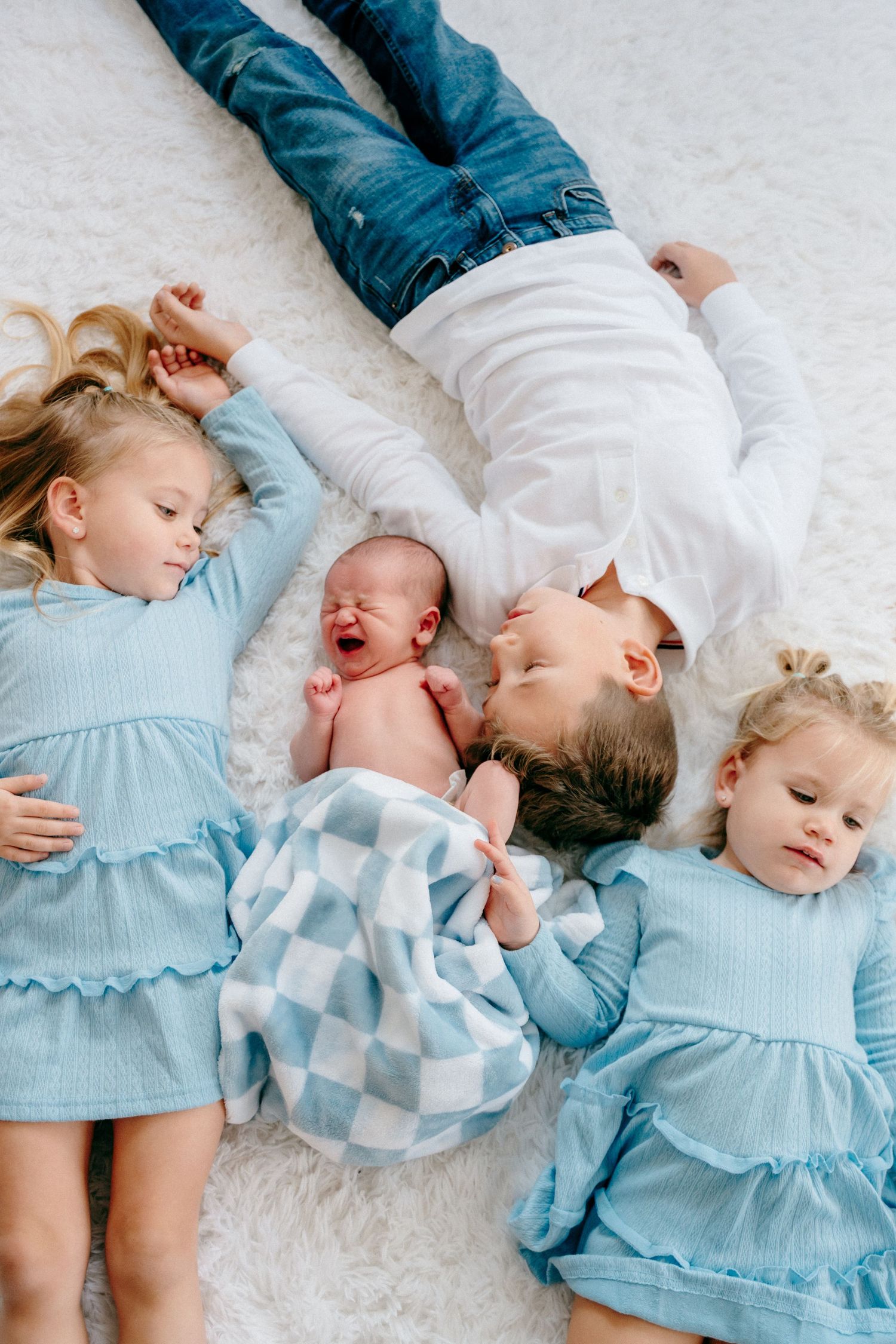 Children in coordinating blue and white outfits lying together on plush white carpet.