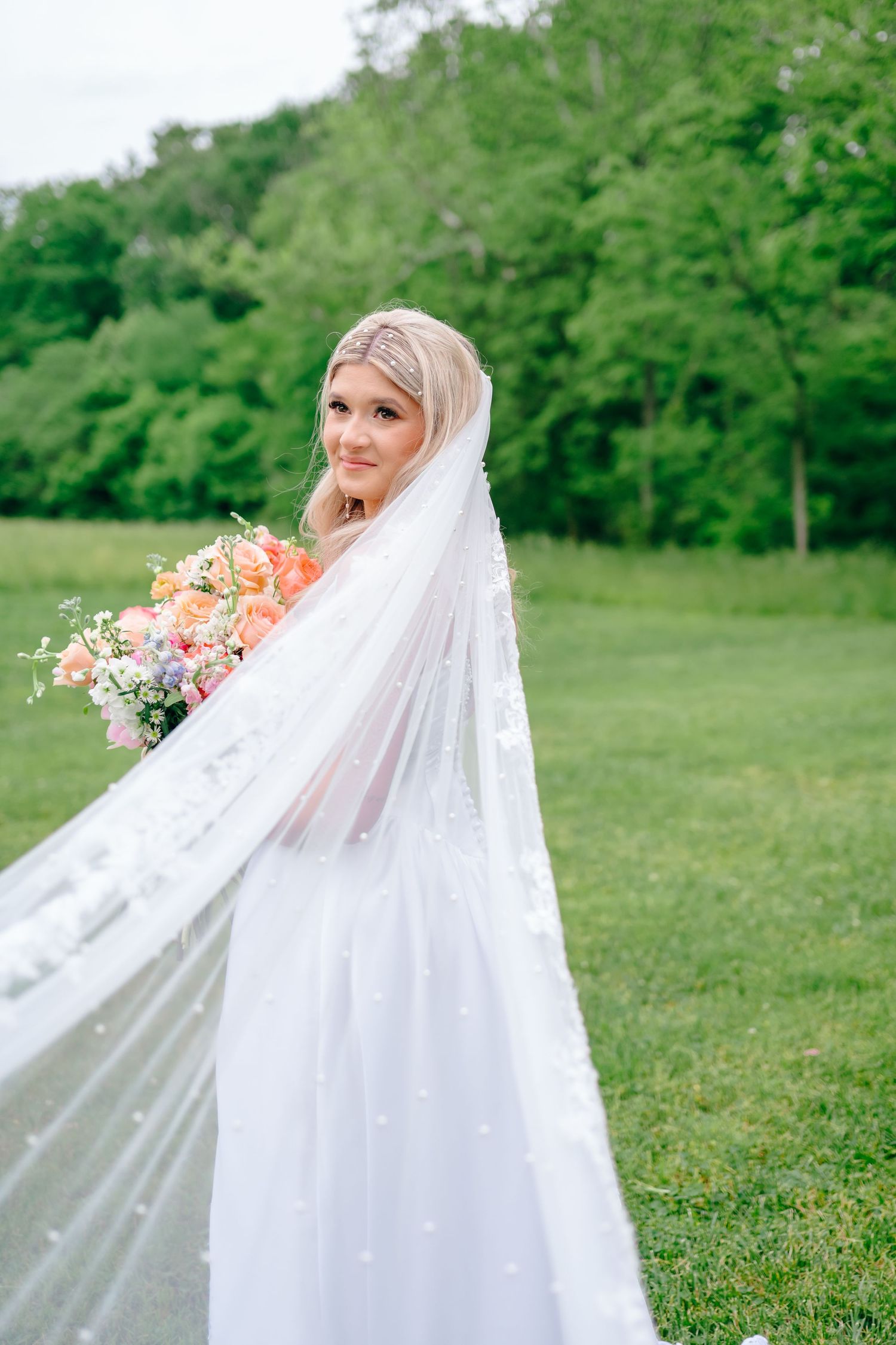 Ethereal bridal portraits with flowing veil against green outdoor backdrop.