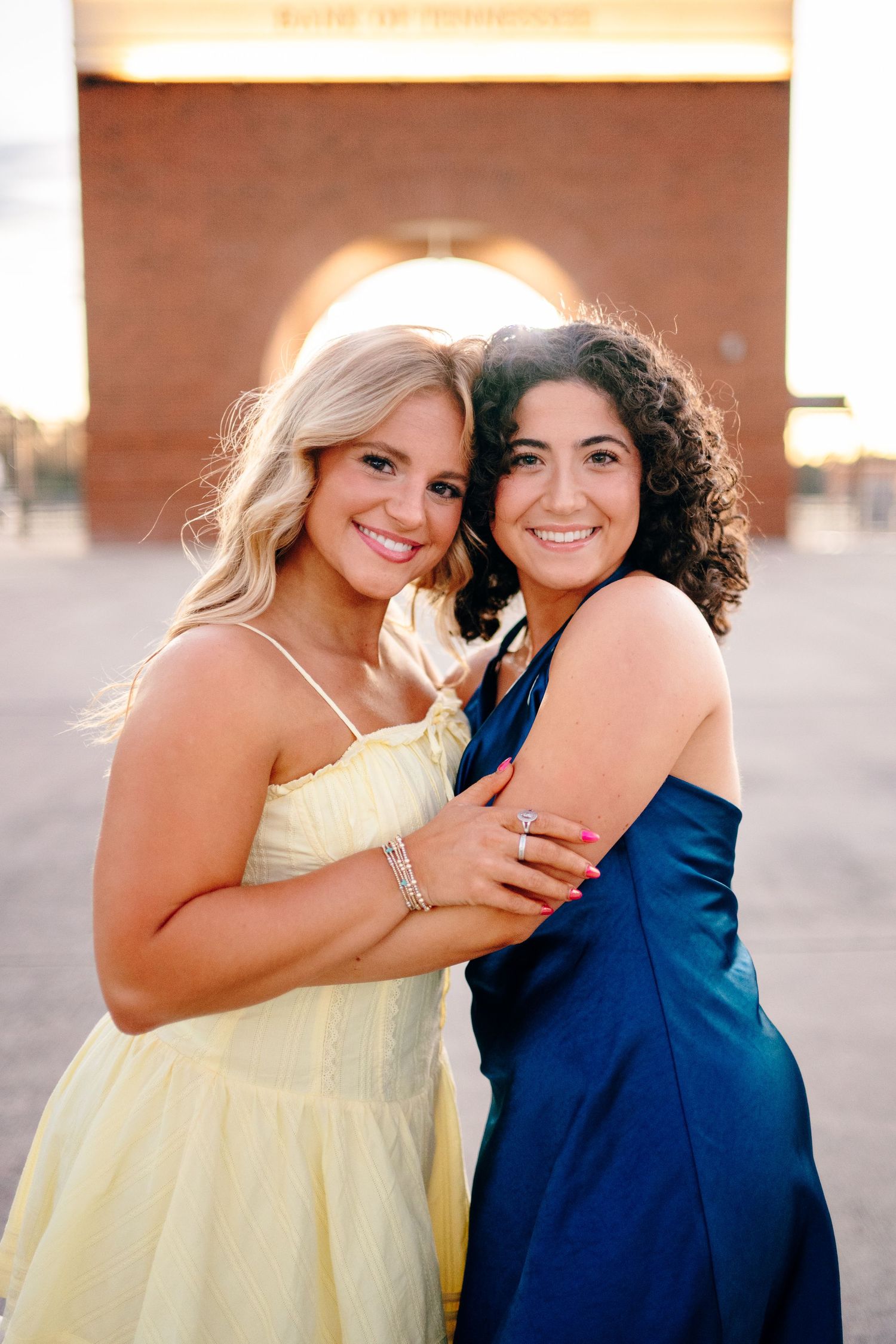 Two friends in contrasting yellow and navy dresses embrace while celebrating graduation.