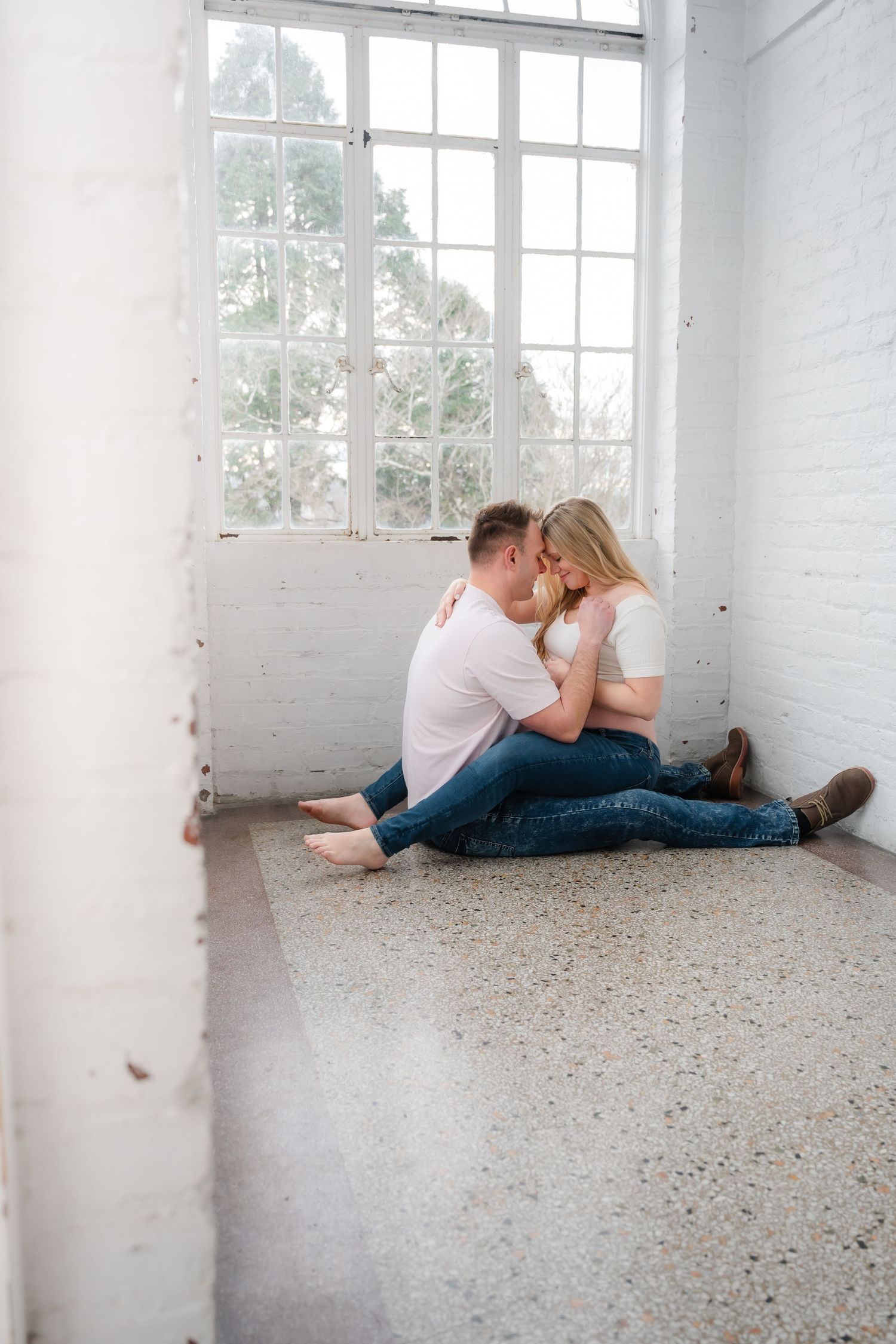 Intimate maternity photos of couple on terrazzo floor in bright white room.