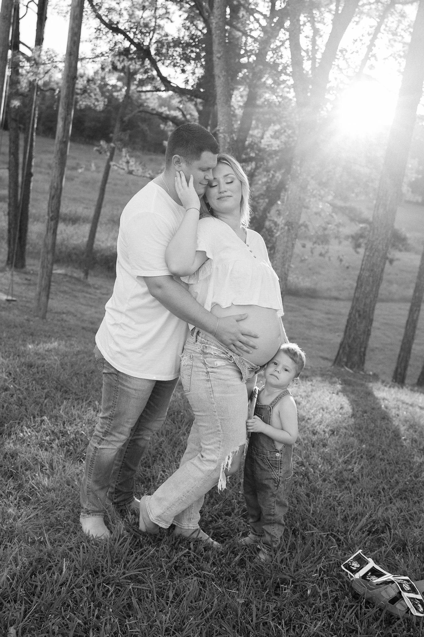 Black and white family portrait session in wooded setting during golden hour.