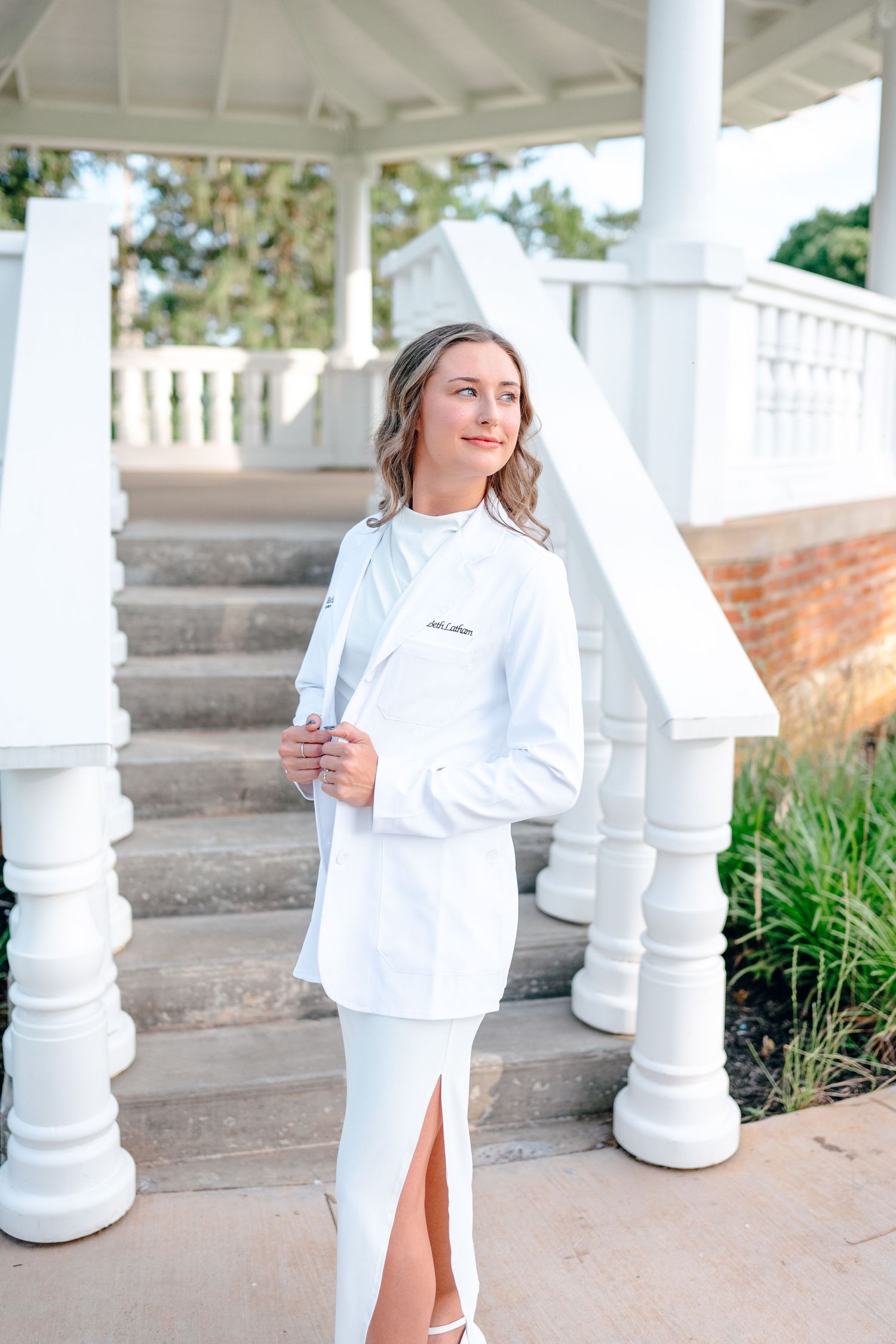Elegant graduation photos in all white attire under a columned pavilion.