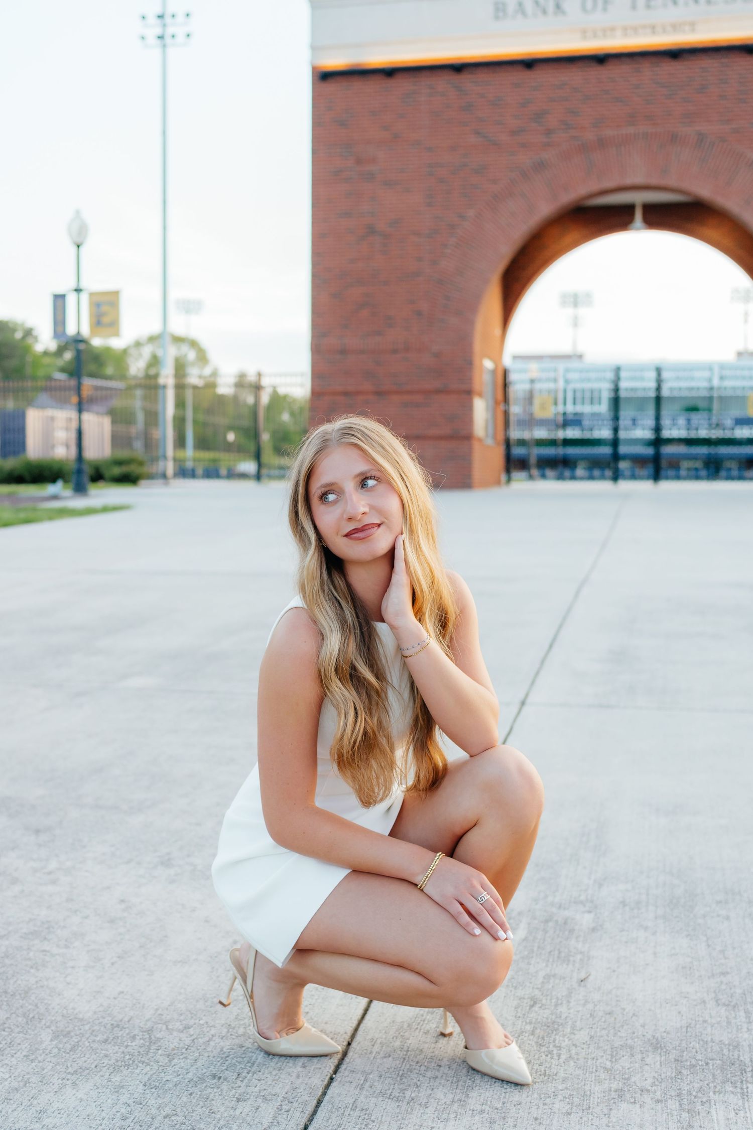 Woman in white dress crouches by brick archway in outdoor urban setting.