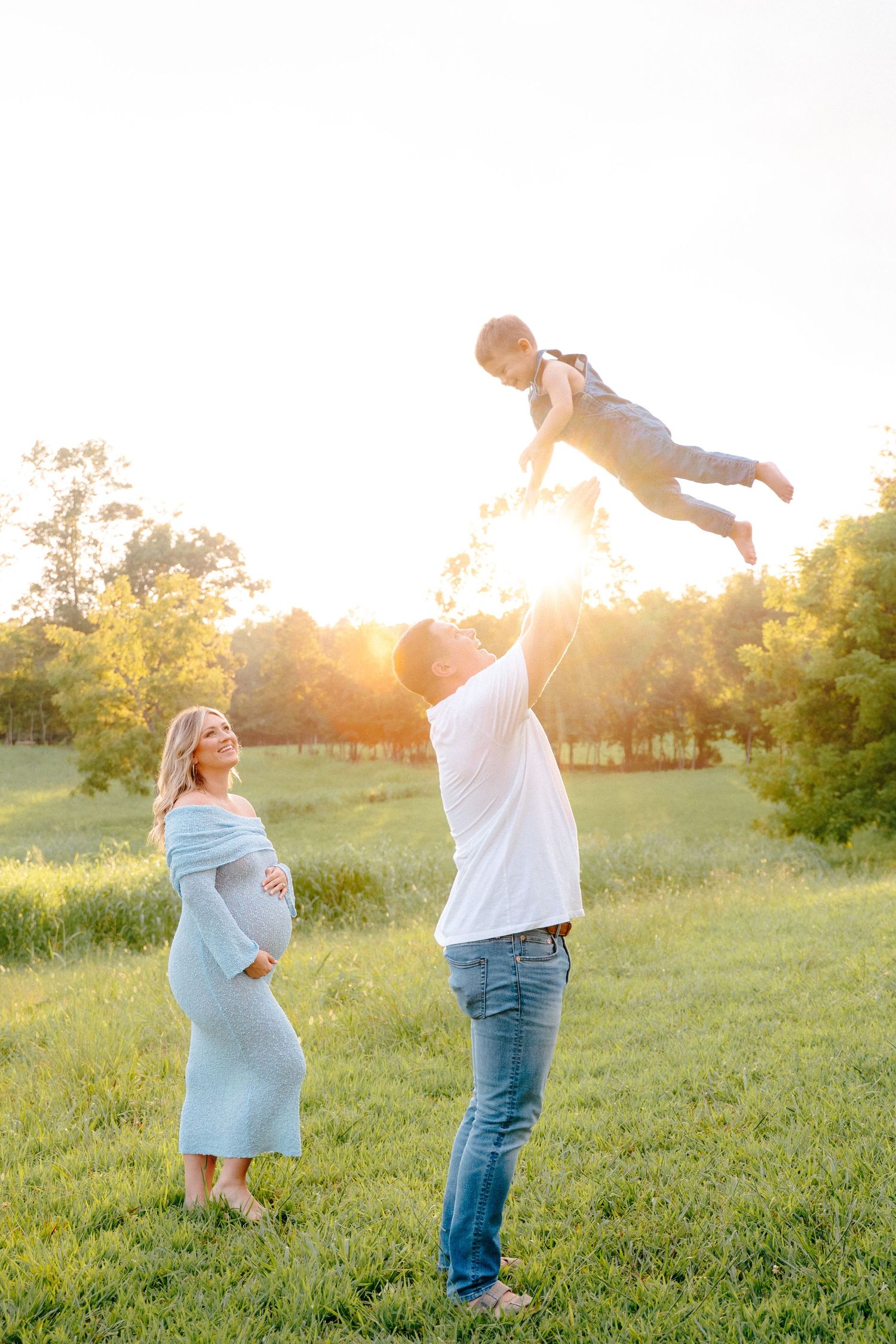 Family plays together in sunlit field during golden hour photo session.