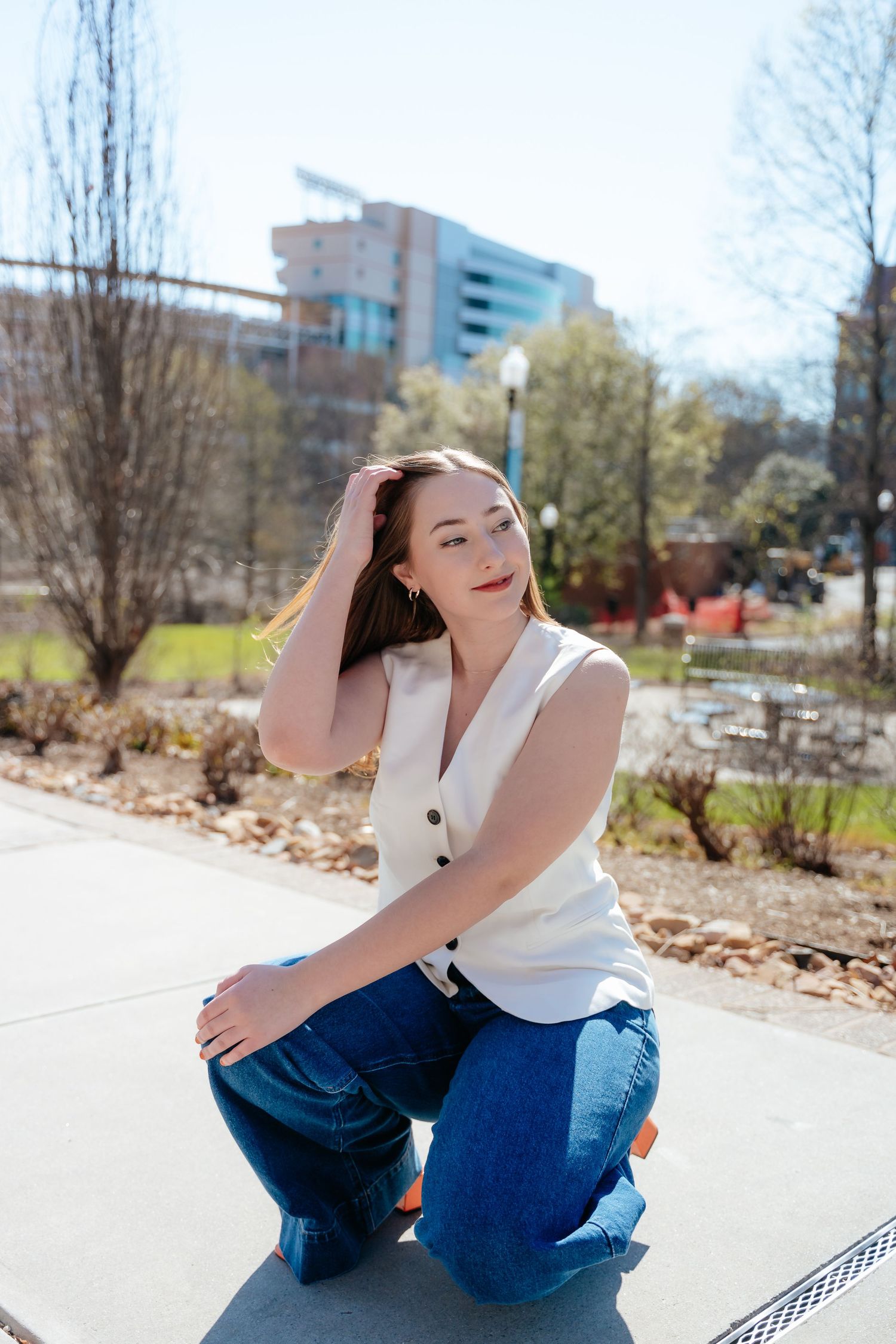 Graduate in white sleeveless top sits casually on outdoor campus steps.