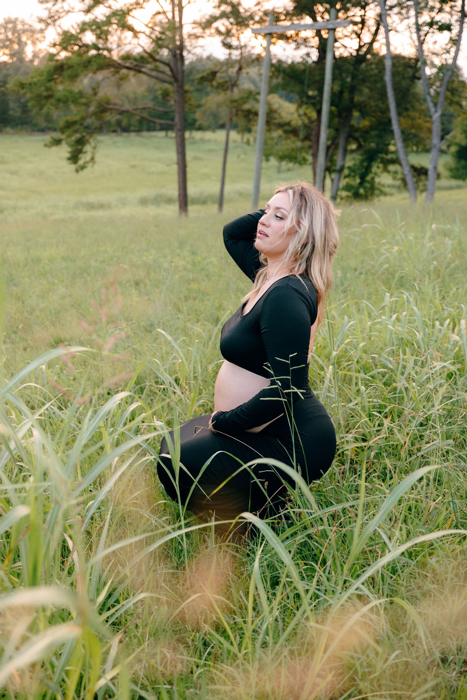 Maternity photos in tall grass field during golden hour.