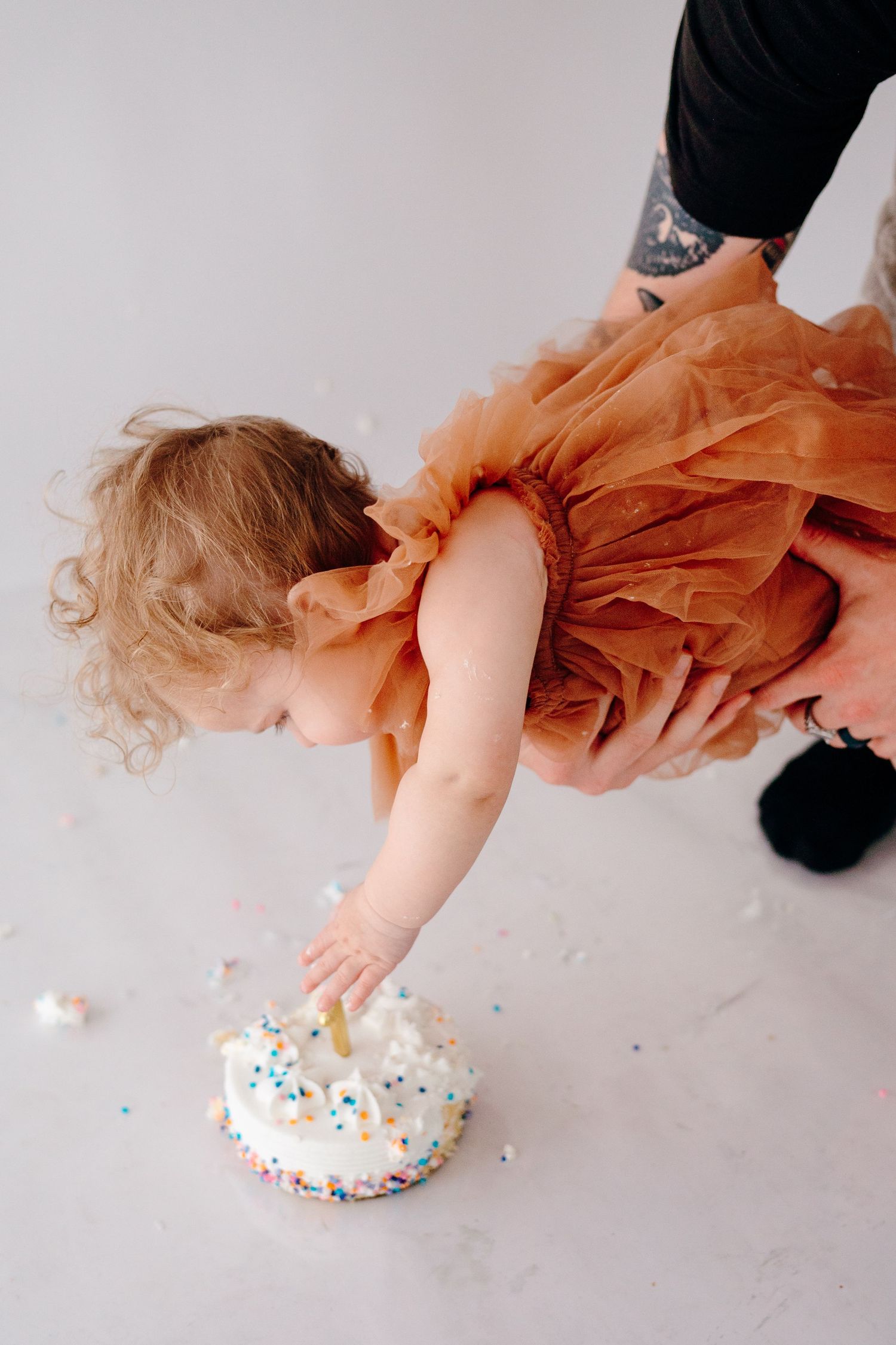 Baby in peach dress reaches down to touch white frosted cake.