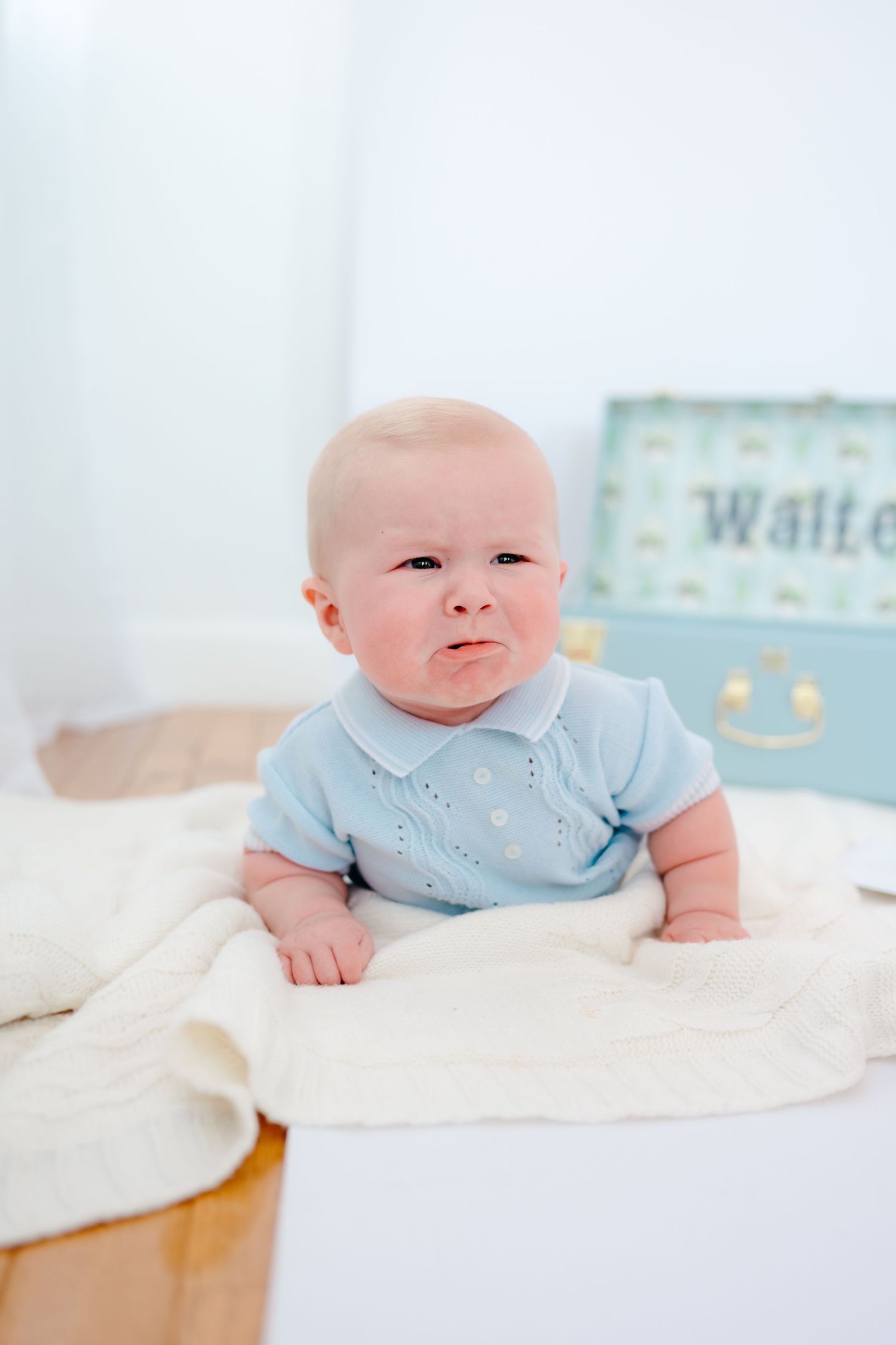 Baby wearing light blue onesie lying on white blanket in progression of poses.