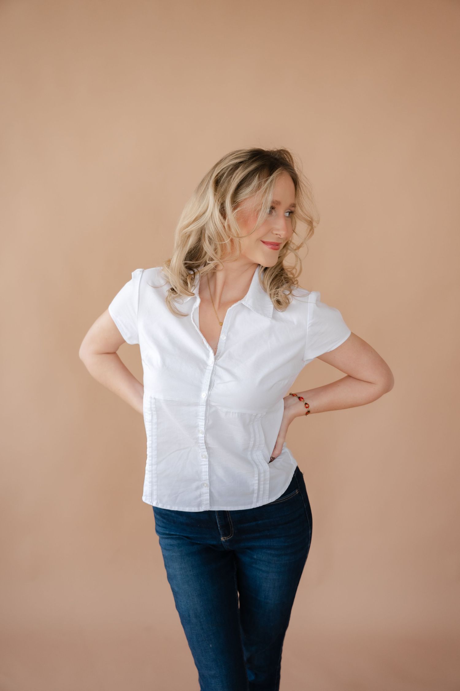 Four fashion poses showing a white button-down shirt paired with dark jeans against a neutral beige background.