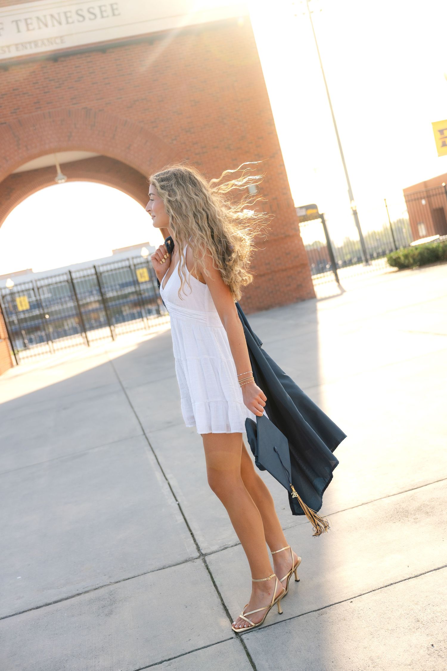 Blonde woman in white dress holding graduation cap and gown outside University of Tennessee building.