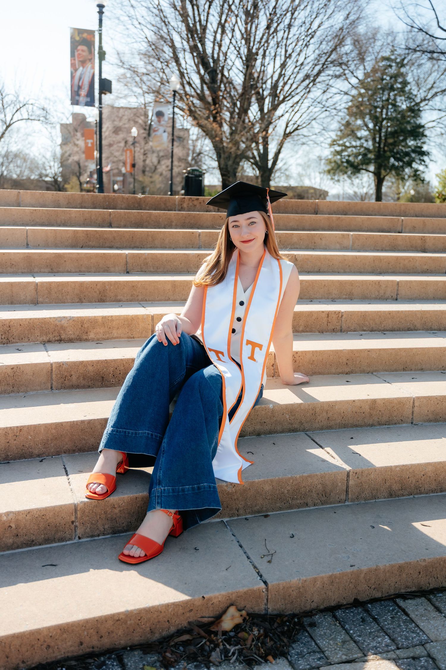 Graduate in academic regalia lounges on concrete campus steps.