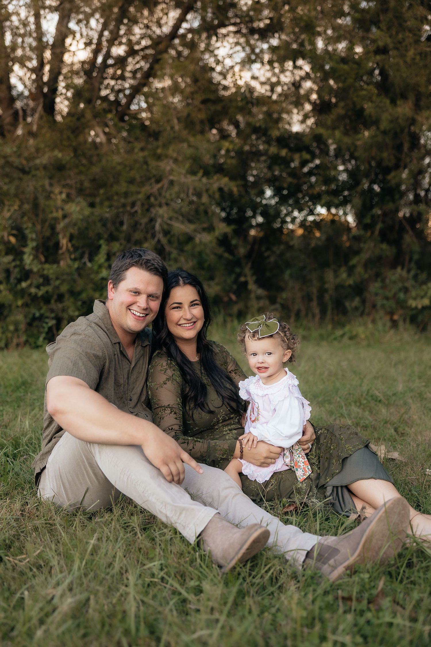 Family relaxing together on grass during outdoor photo session.