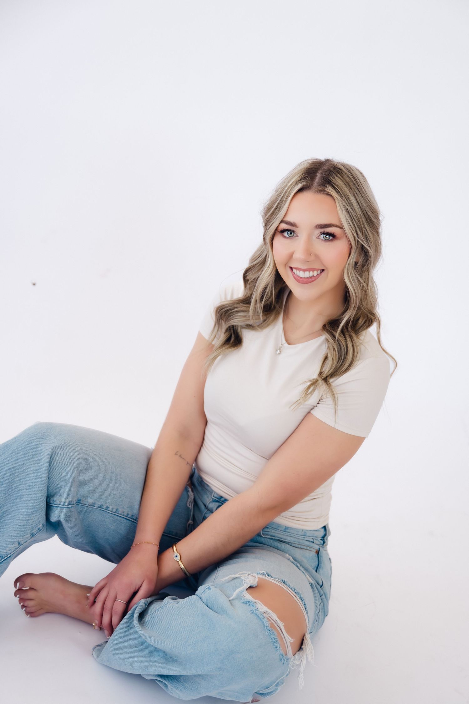 A casual portrait series showing a relaxed pose in light denim jeans and white top against a bright studio backdrop.