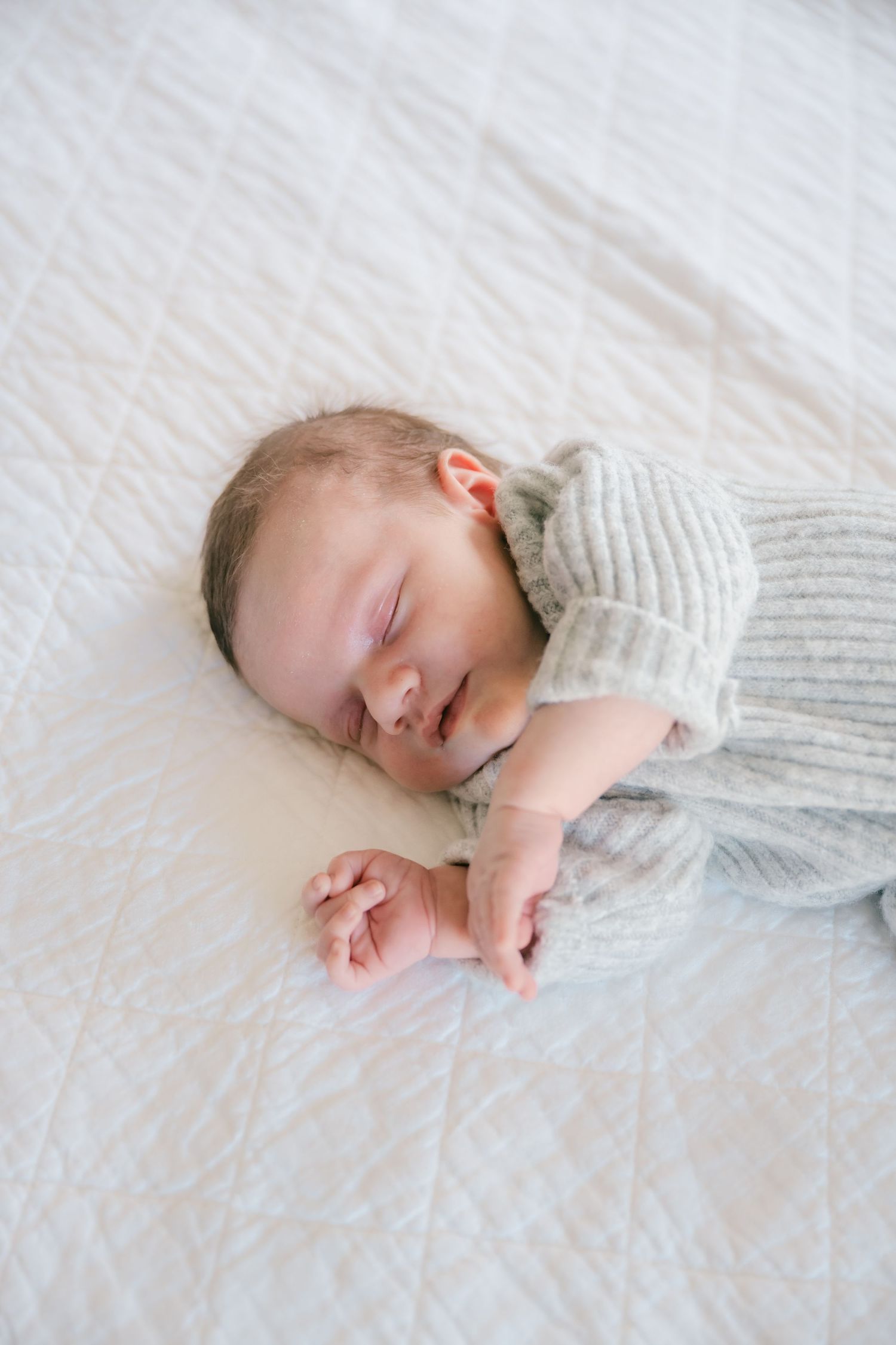 Sleeping newborn wrapped in soft white knitted blanket on textured bedding.