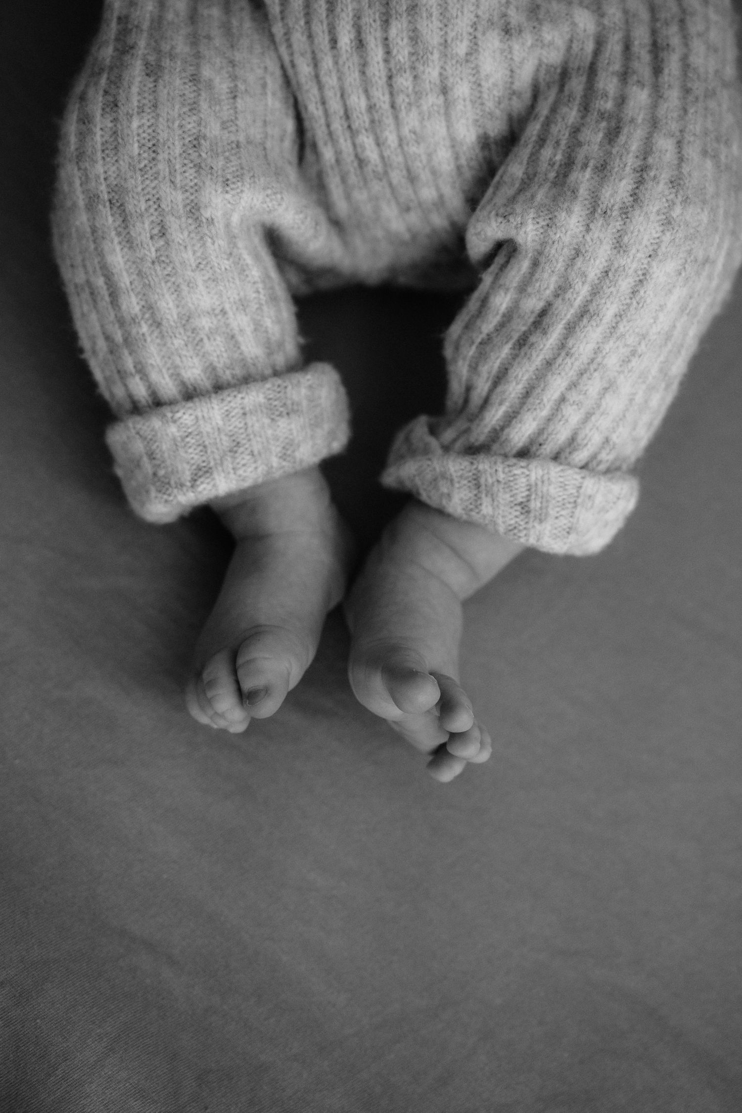 Close-up of tiny feet in gray knit pants against dark background.