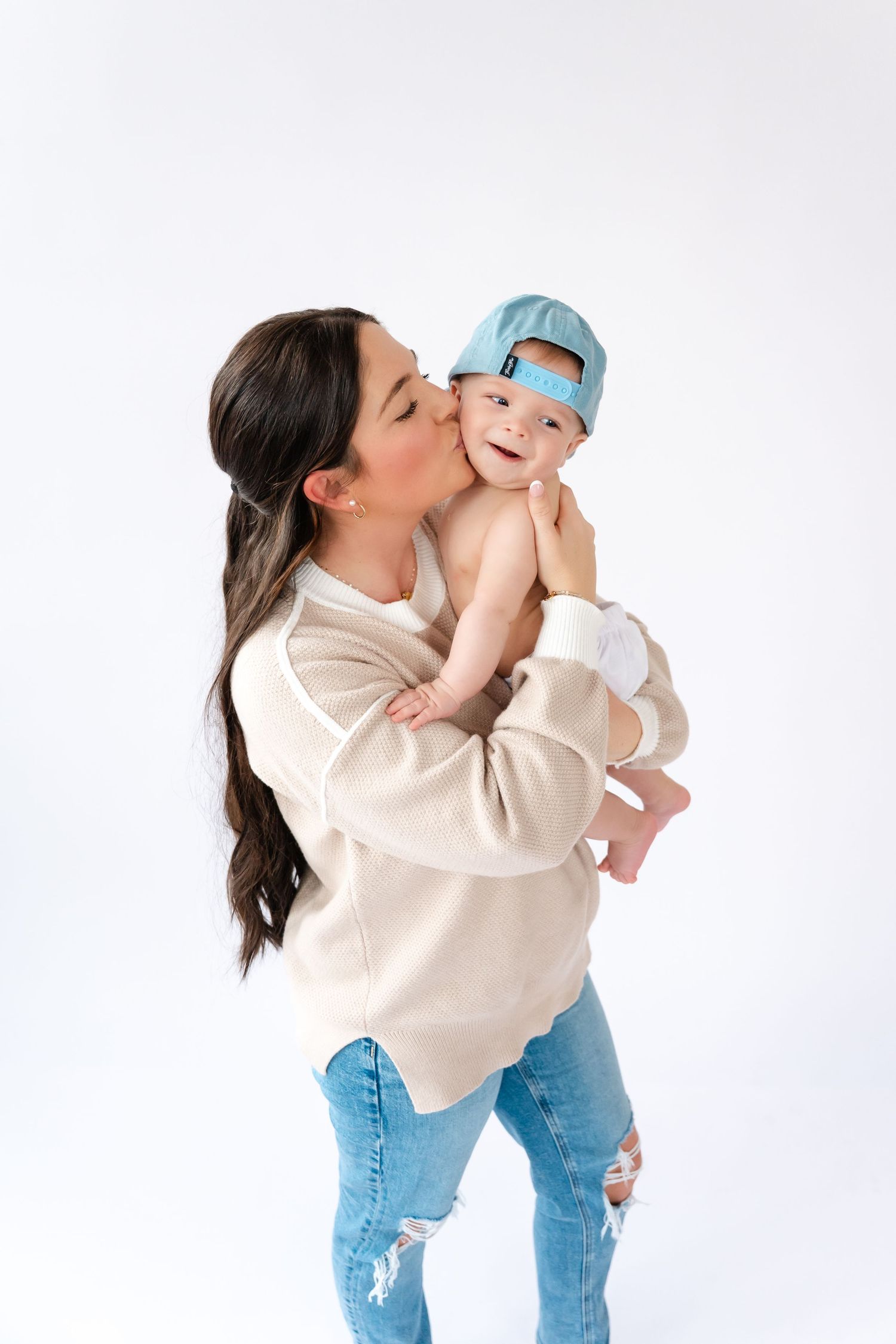 Mother in cream sweater and jeans playing with baby in candid lifestyle photos against white background.
