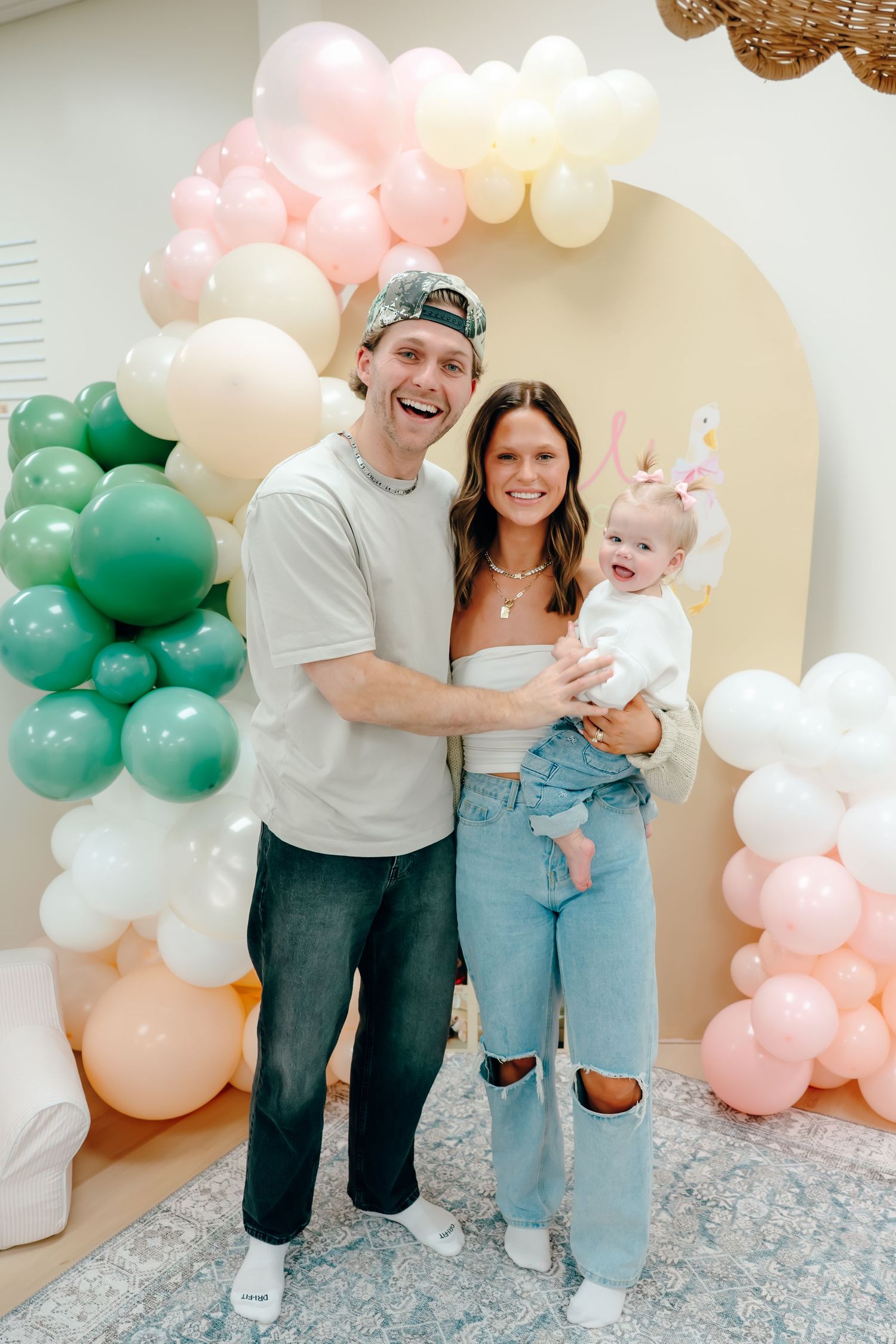 Family poses together against balloon arch backdrop in casual denim and white outfits for celebration photos.