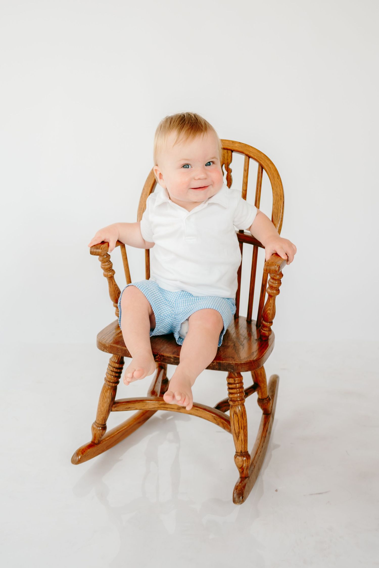 Baby in white shirt and blue shorts sitting in a wooden rocking chair.