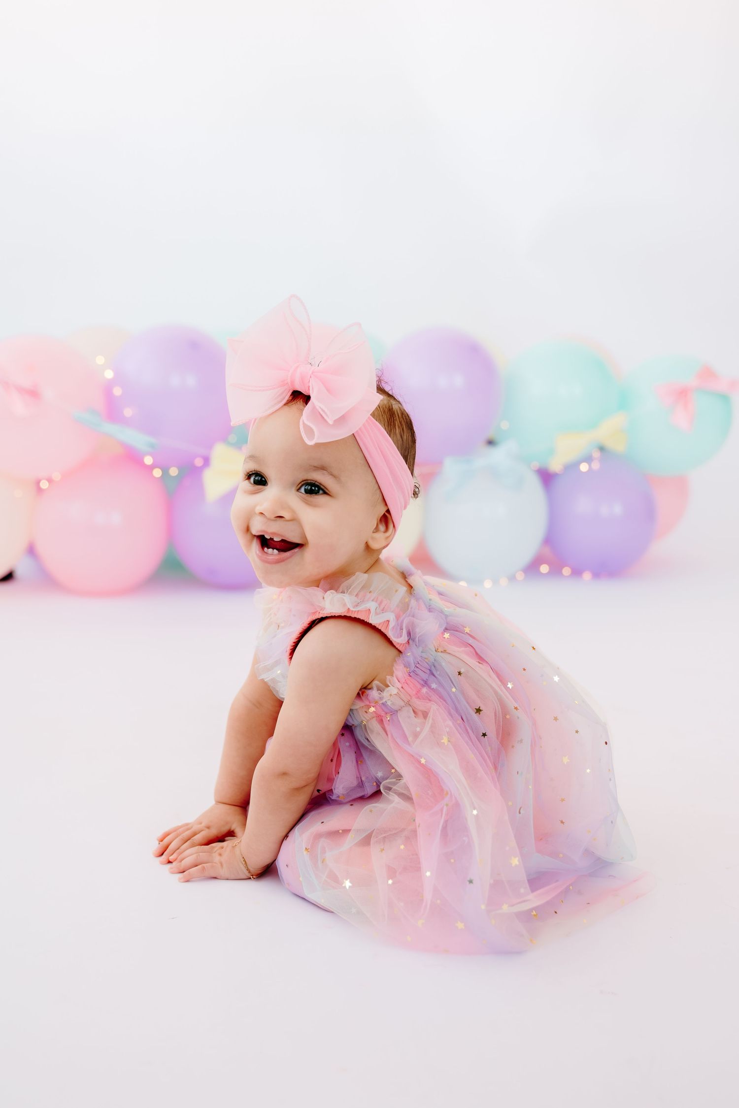 Baby in tulle dress lying among pastel balloons during photo session.