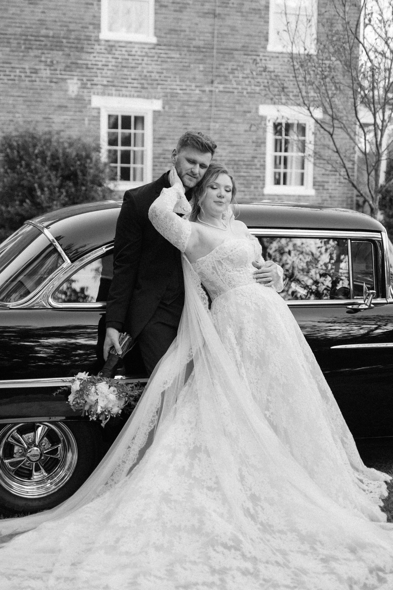 A romantic wedding photo series featuring a classic car and flowing white wedding dress against a brick building.