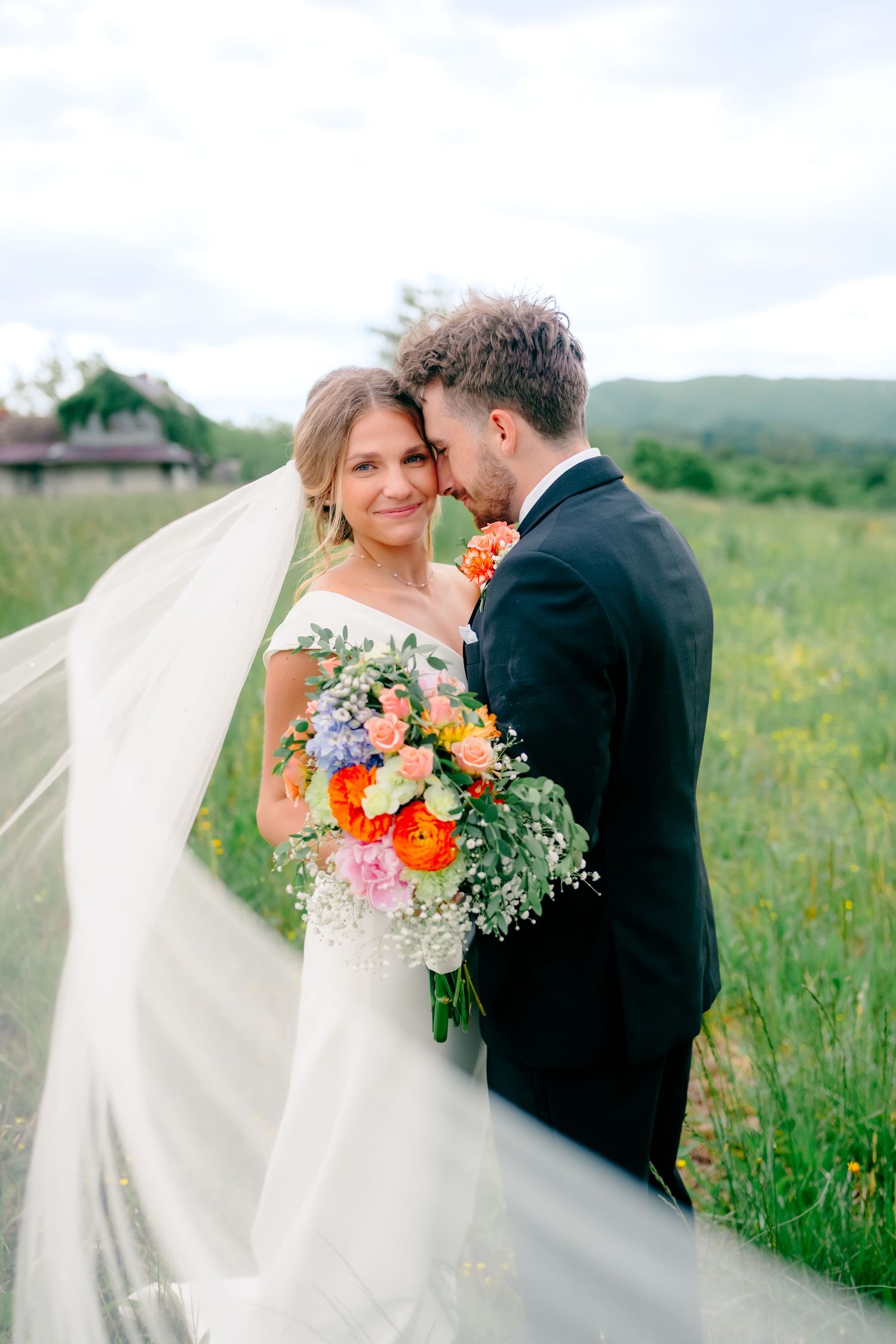 Couple shares intimate moment in wildflower field with dramatic veil and colorful bouquet.