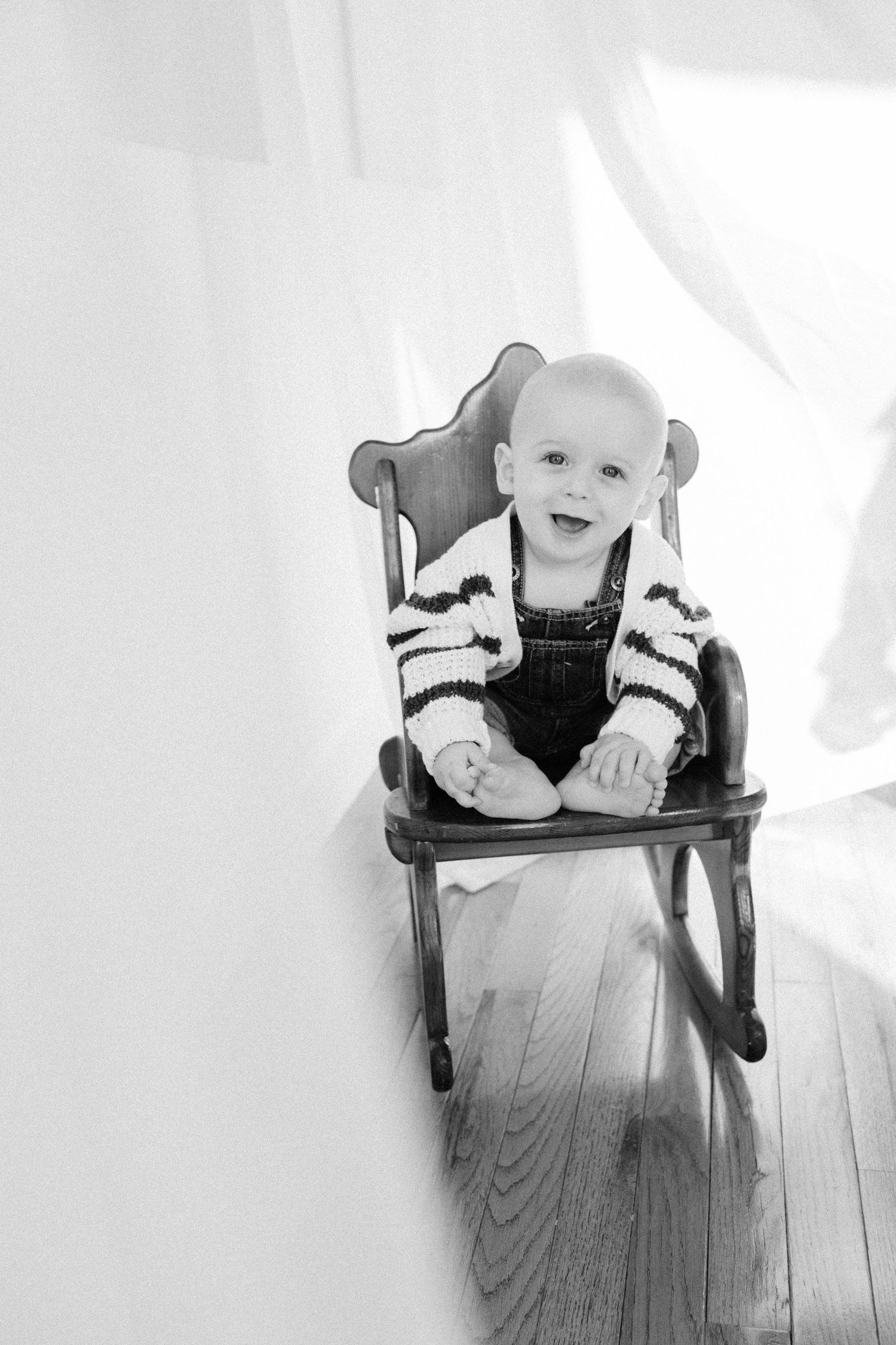 Black and white photo sequence showing a baby sitting in a wooden high chair, smiling and moving in four progressive shots.