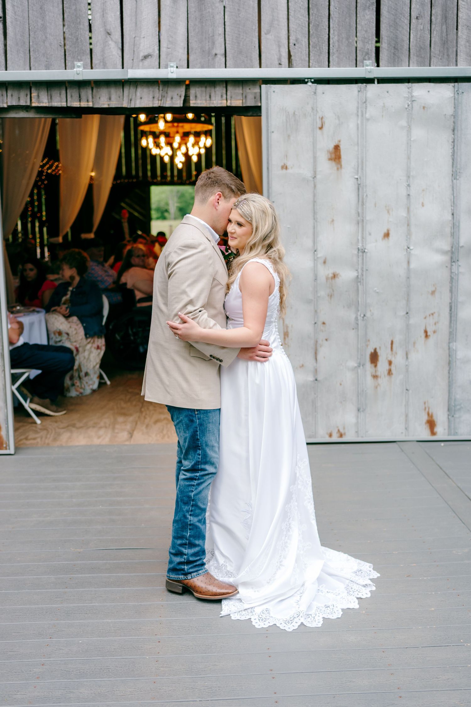 Romantic dance moment at rustic barn wedding venue with chandelier.