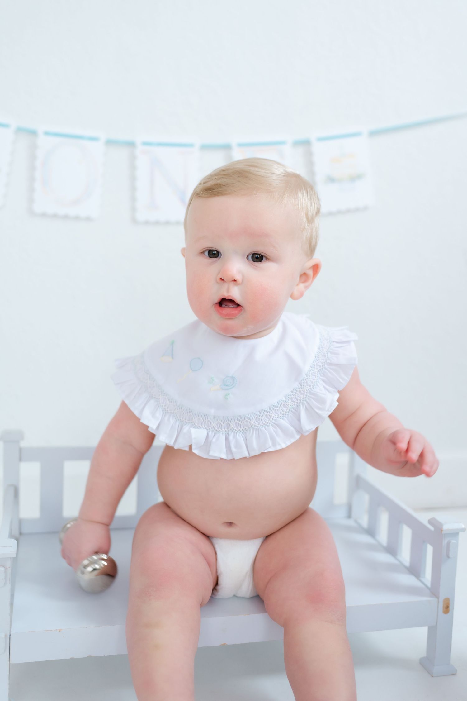 Baby wearing white ruffled collar sits on white bench in three progressive poses showing movement and expression.