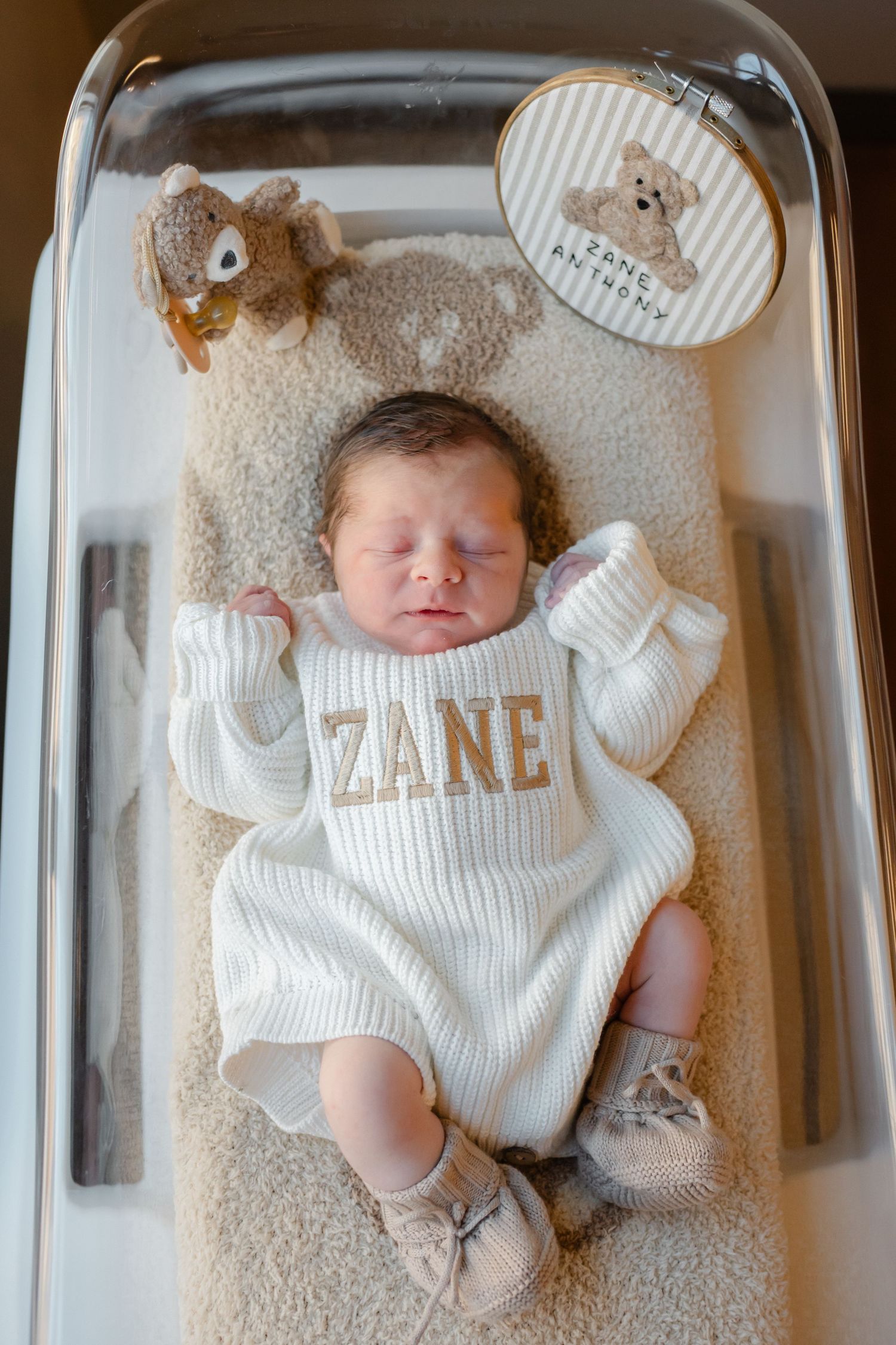 Newborn baby sleeping in hospital bassinet wearing white outfit with name 'Zeke' displayed.