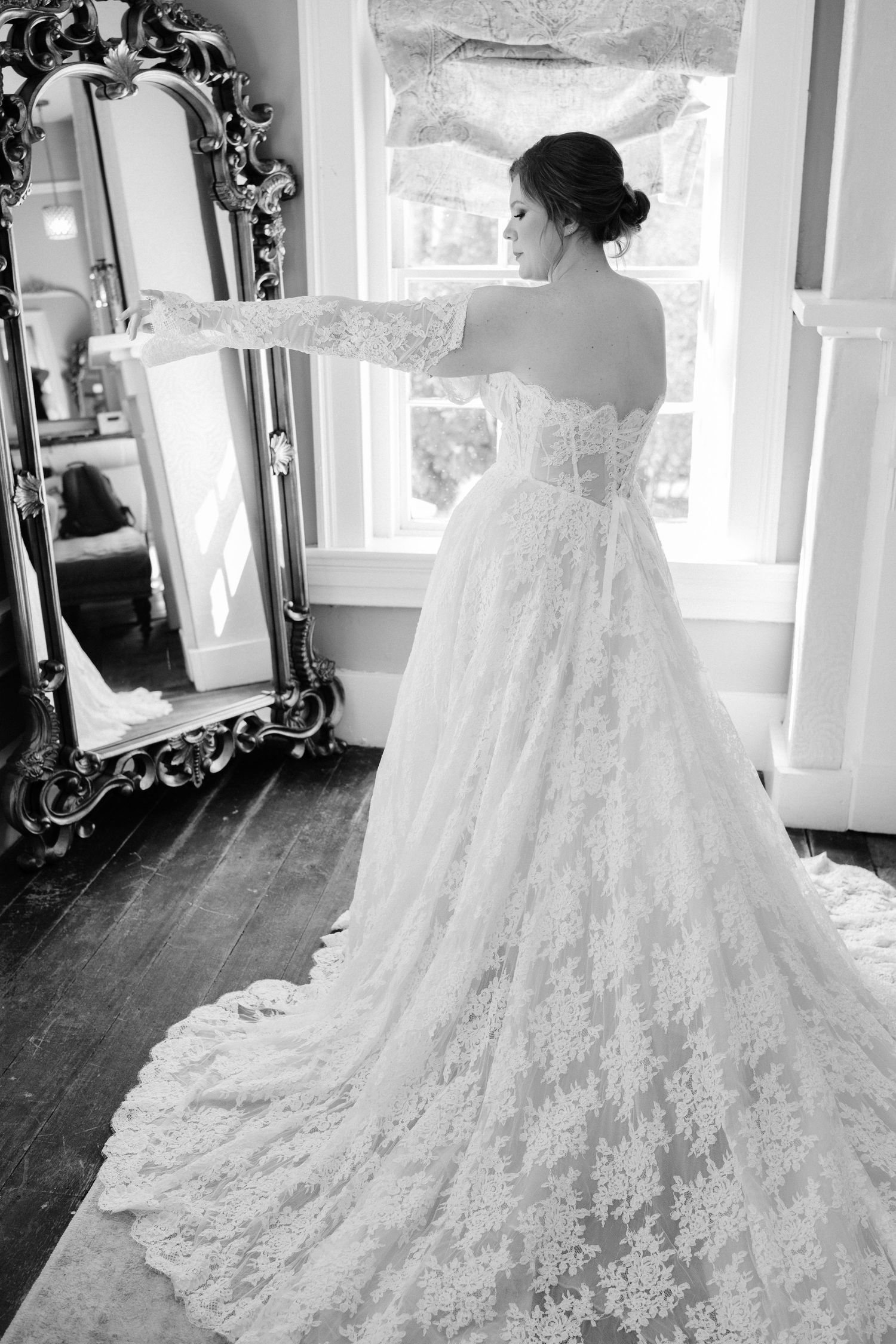 Stunning lace wedding dress with cathedral train displayed in bridal suite with ornate mirror.