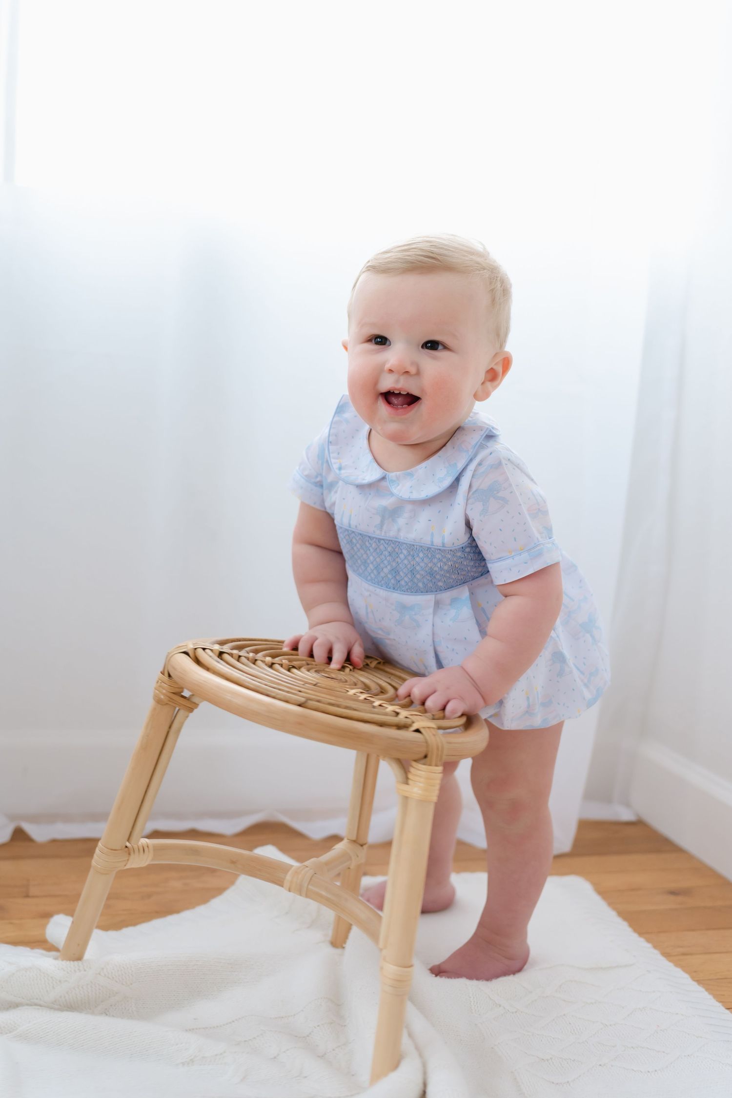 A baby in a light blue outfit stands at a wooden stool on a white rug, showing three progressive stages of movement.