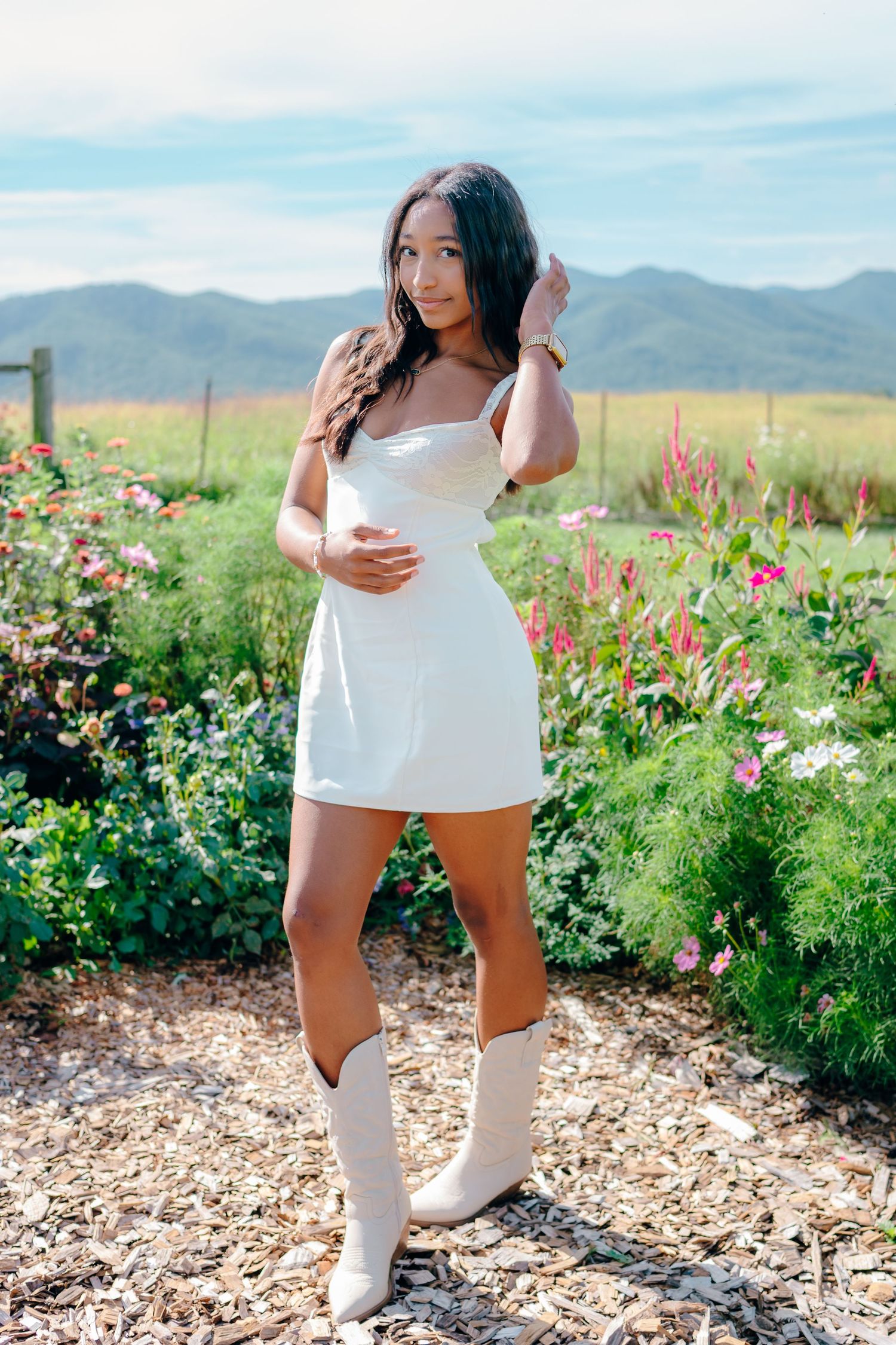 Fashion photography in white outfit against mountain landscape with colorful wildflowers.