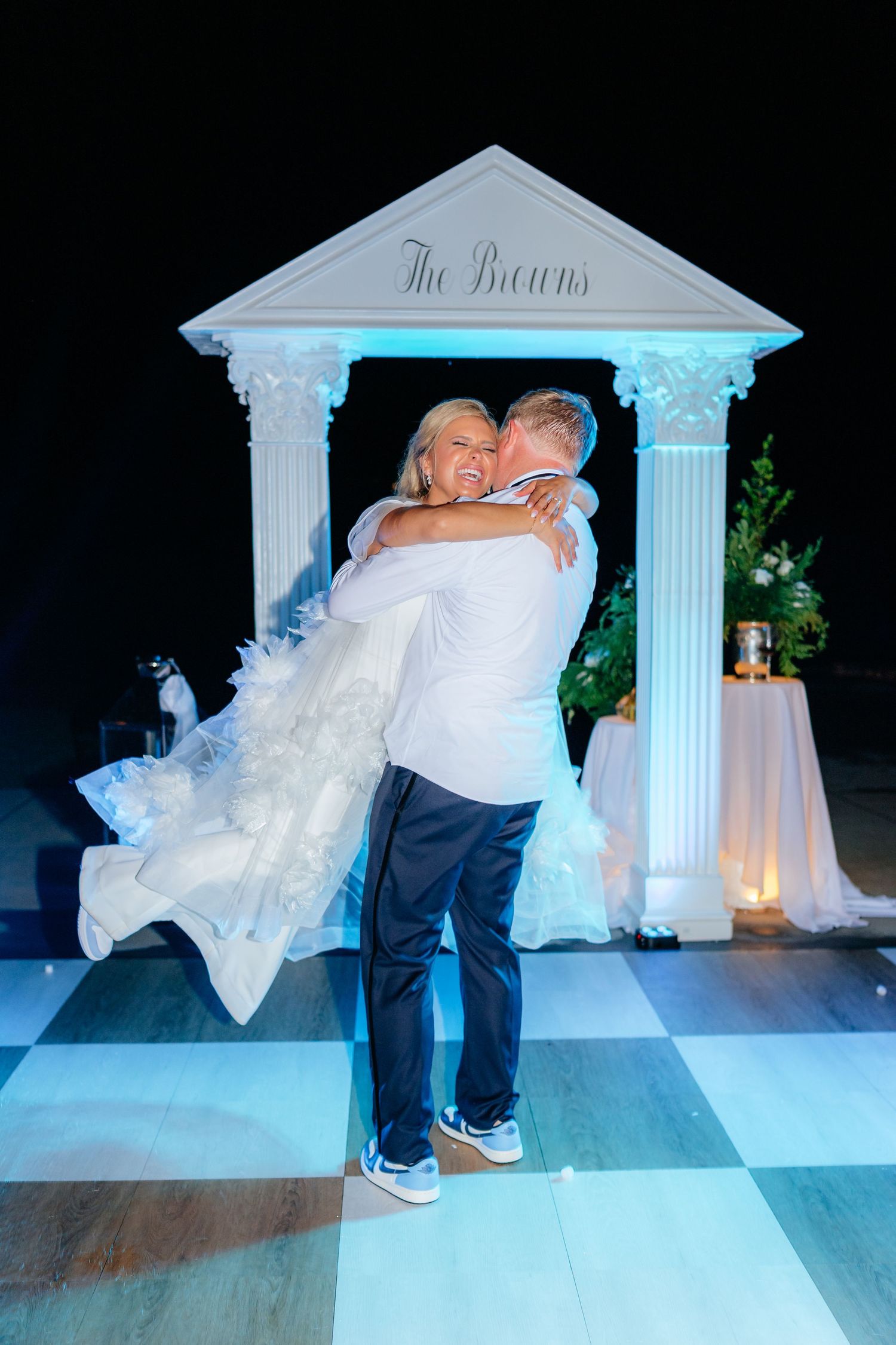 Couple performs playful dance moves under decorative white columns at reception.