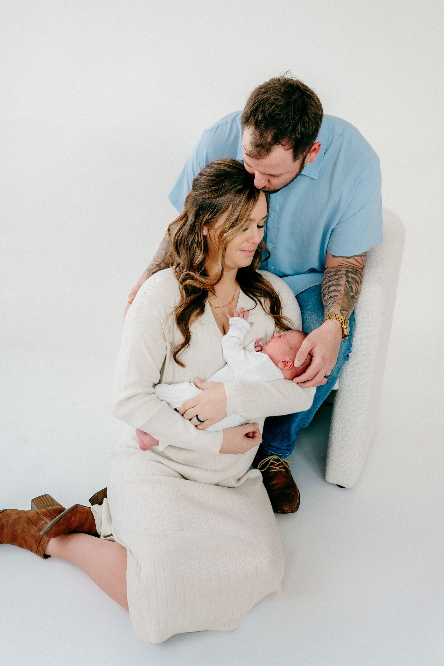 Family shares intimate moment on white background during newborn photoshoot.