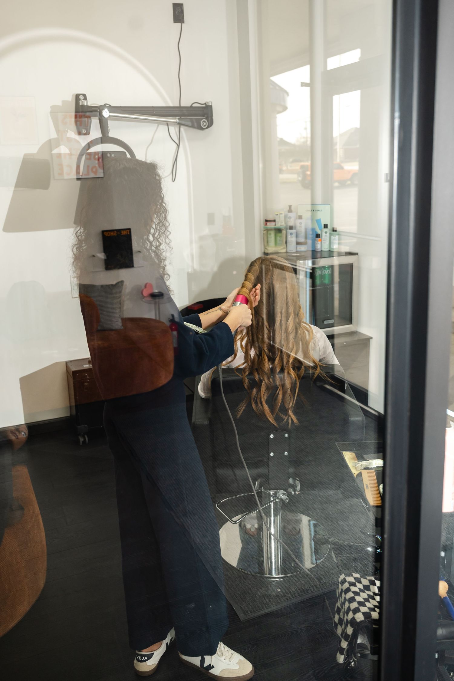 Behind-the-scenes view of a hair styling session in a modern salon interior with natural lighting.