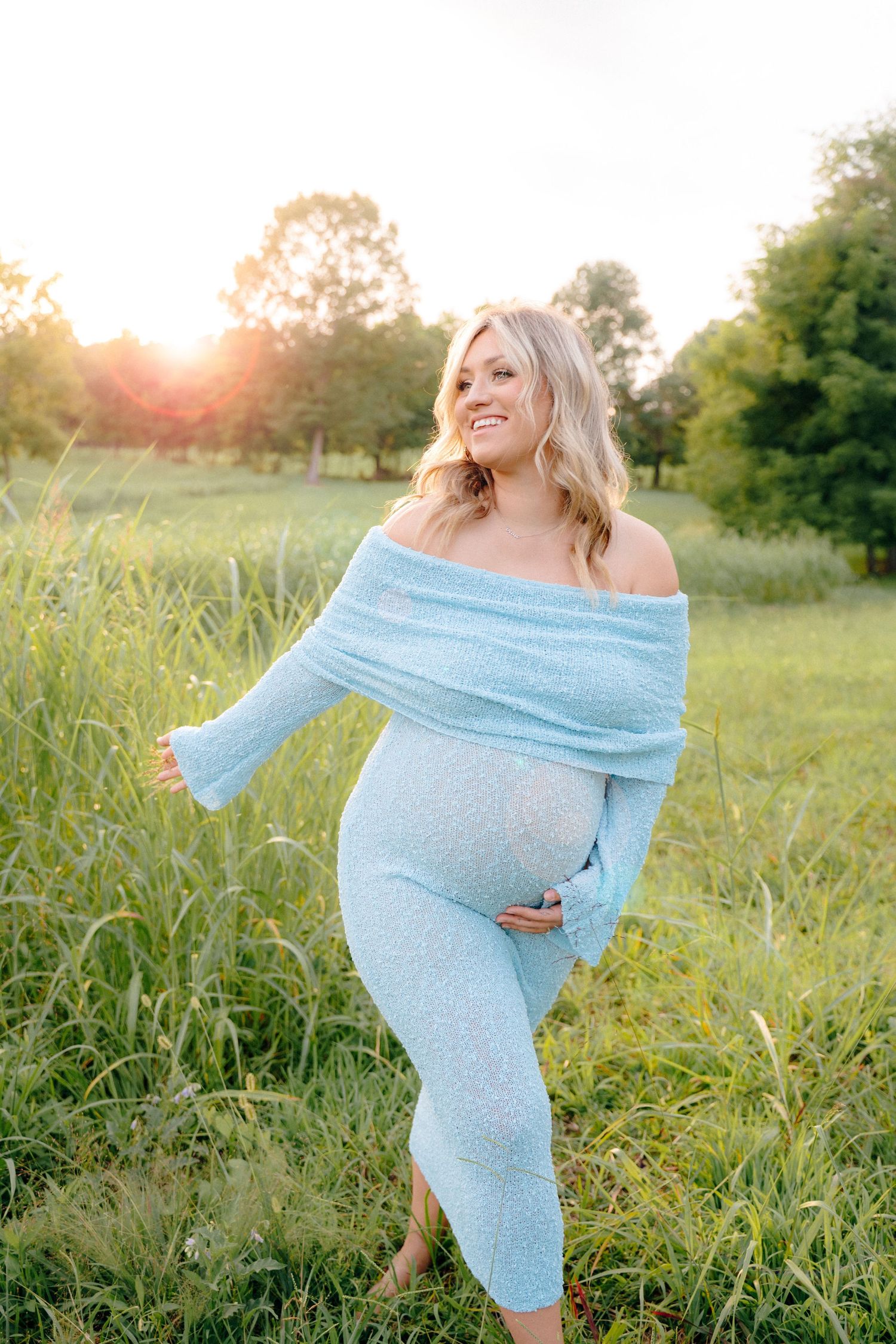 Joyful maternity photo captured in golden sunlight with woman wearing blue dress.