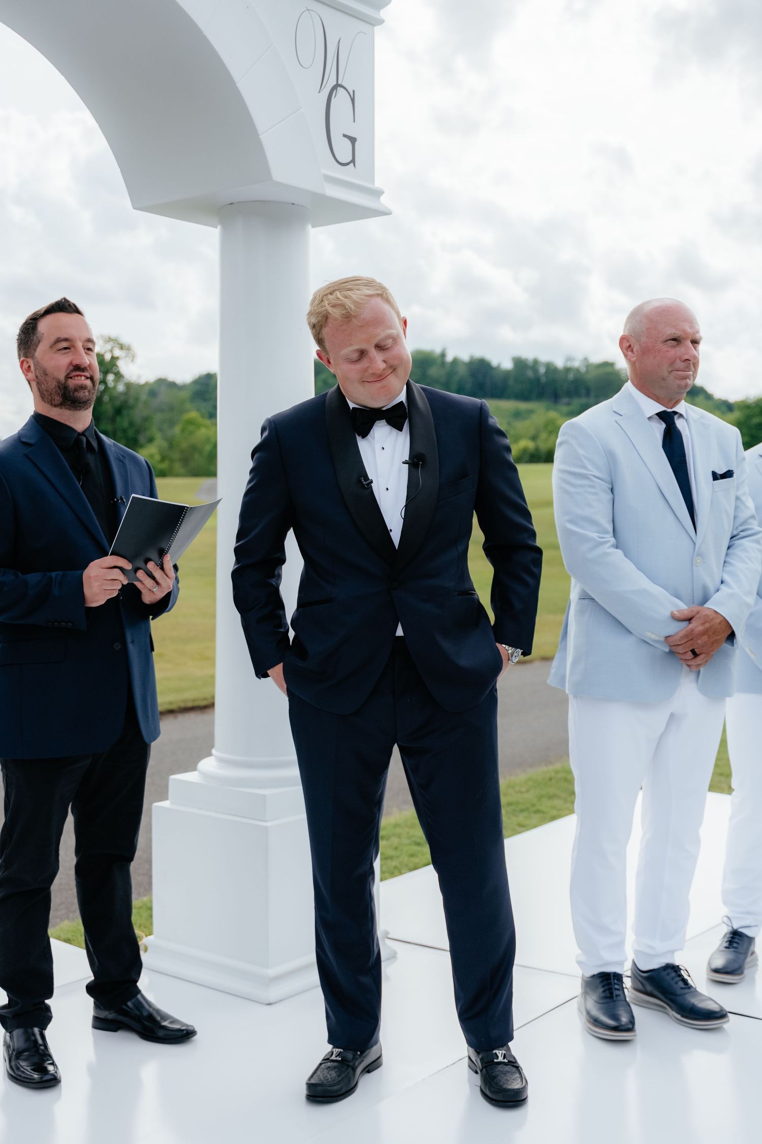 Groomsmen in dark suits and white tuxedos pose casually against white pillars.