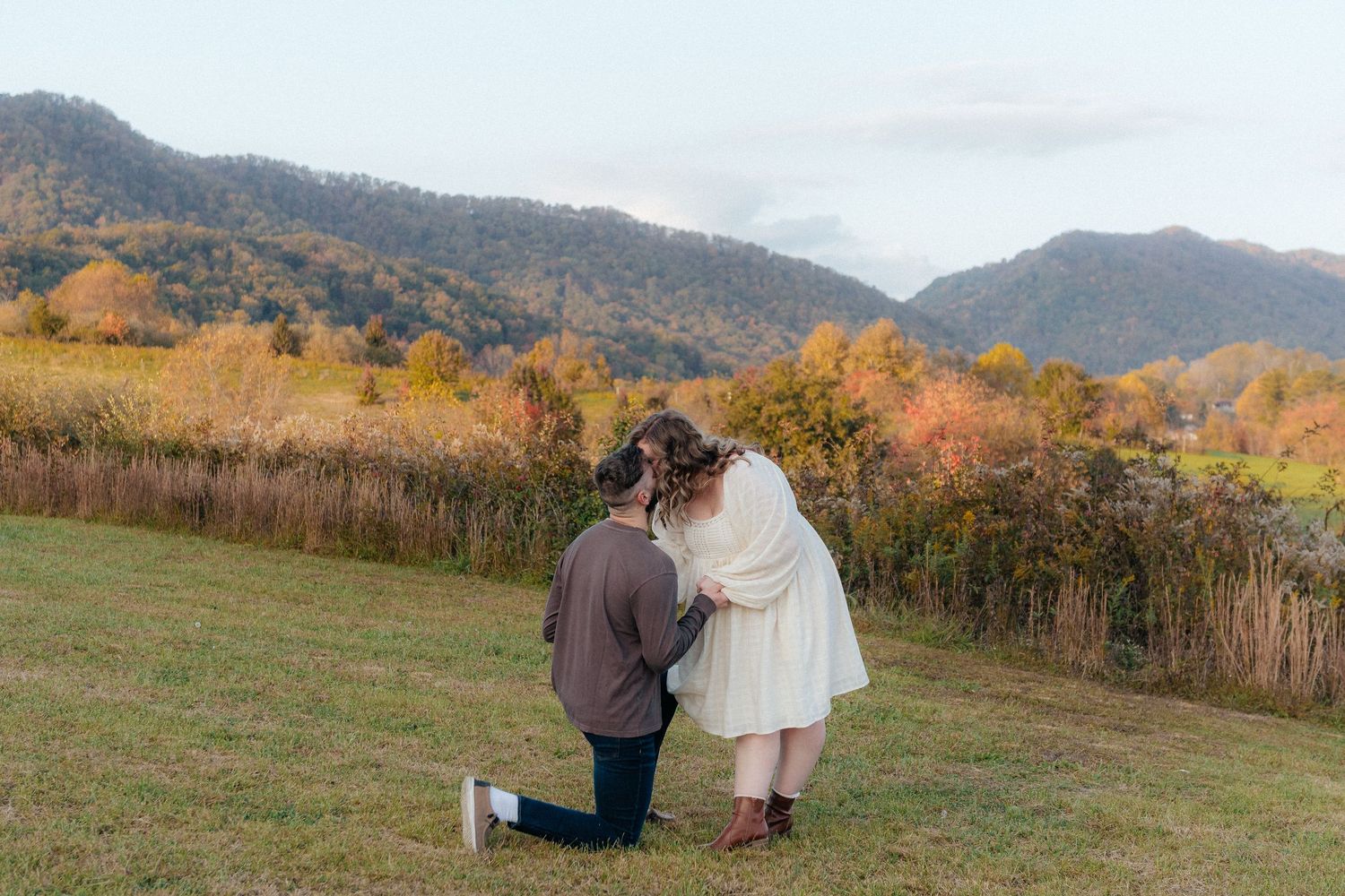 Couple sharing intimate moment on grassy hillside during autumn season.