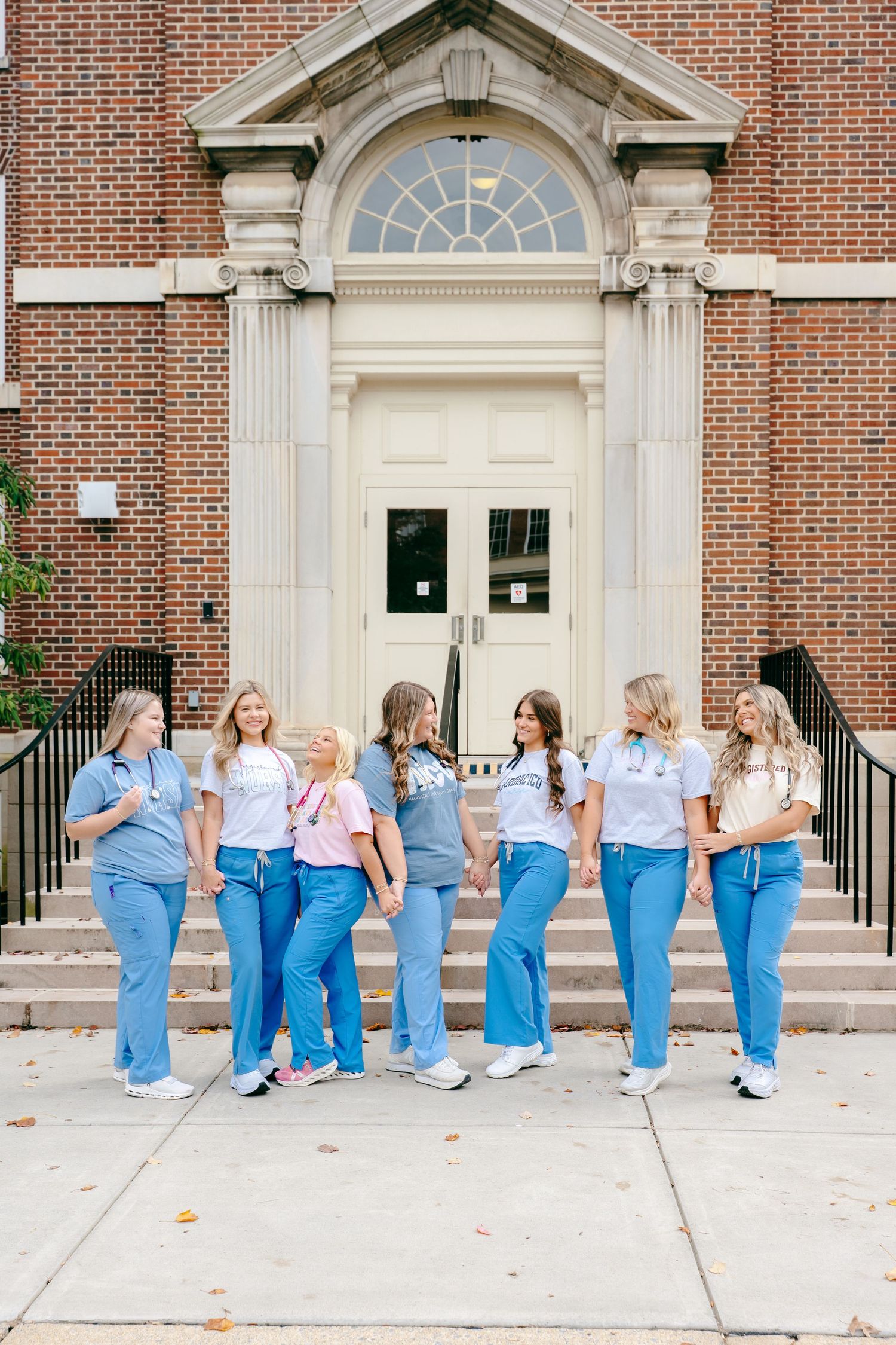 Healthcare students in blue uniforms posing together outside a classic brick building entrance.